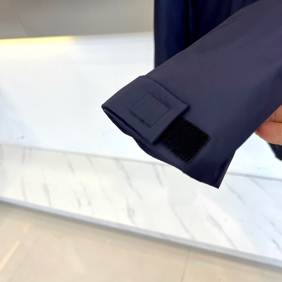 Prad普拉、2025秋冬新品 PRADA科技防护羽绒服。深蓝色连帽设计搭配精密拉链系统，左胸红色织带镶