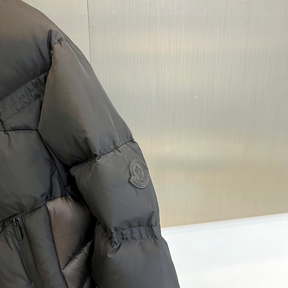Mon蒙口（鹅绒）、2025秋冬新品黑色羽绒服，连帽设计搭配可调节防风系统，左袖饰有反光品牌徽章提升夜间