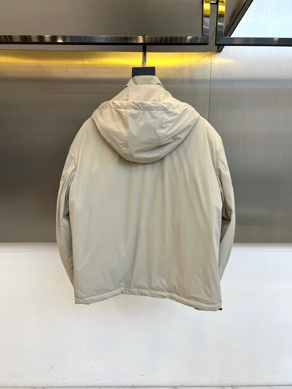 Zegna杰尼亚、2025秋冬新品羽绒服以浅灰质感演绎现代都市美学。这款连帽羽绒服采用极简立体剪裁，前襟