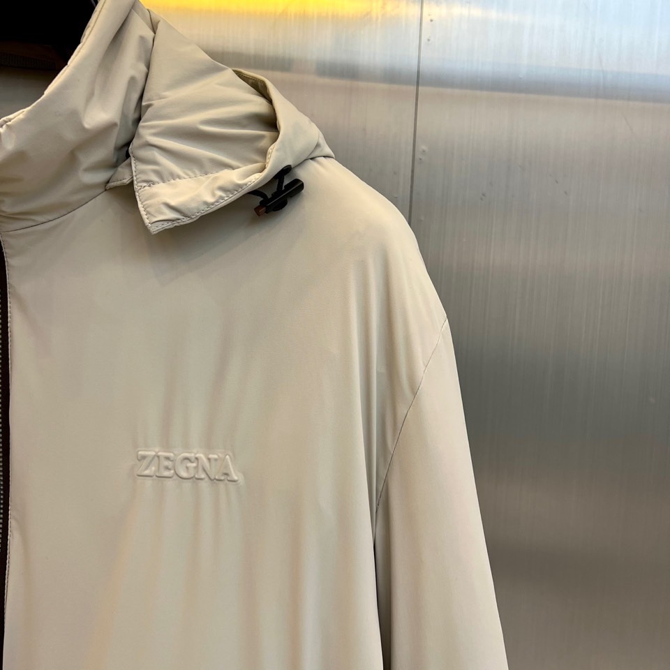 Zegna杰尼亚、2025秋冬新品羽绒服以浅灰质感演绎现代都市美学。这款连帽羽绒服采用极简立体剪裁，前襟