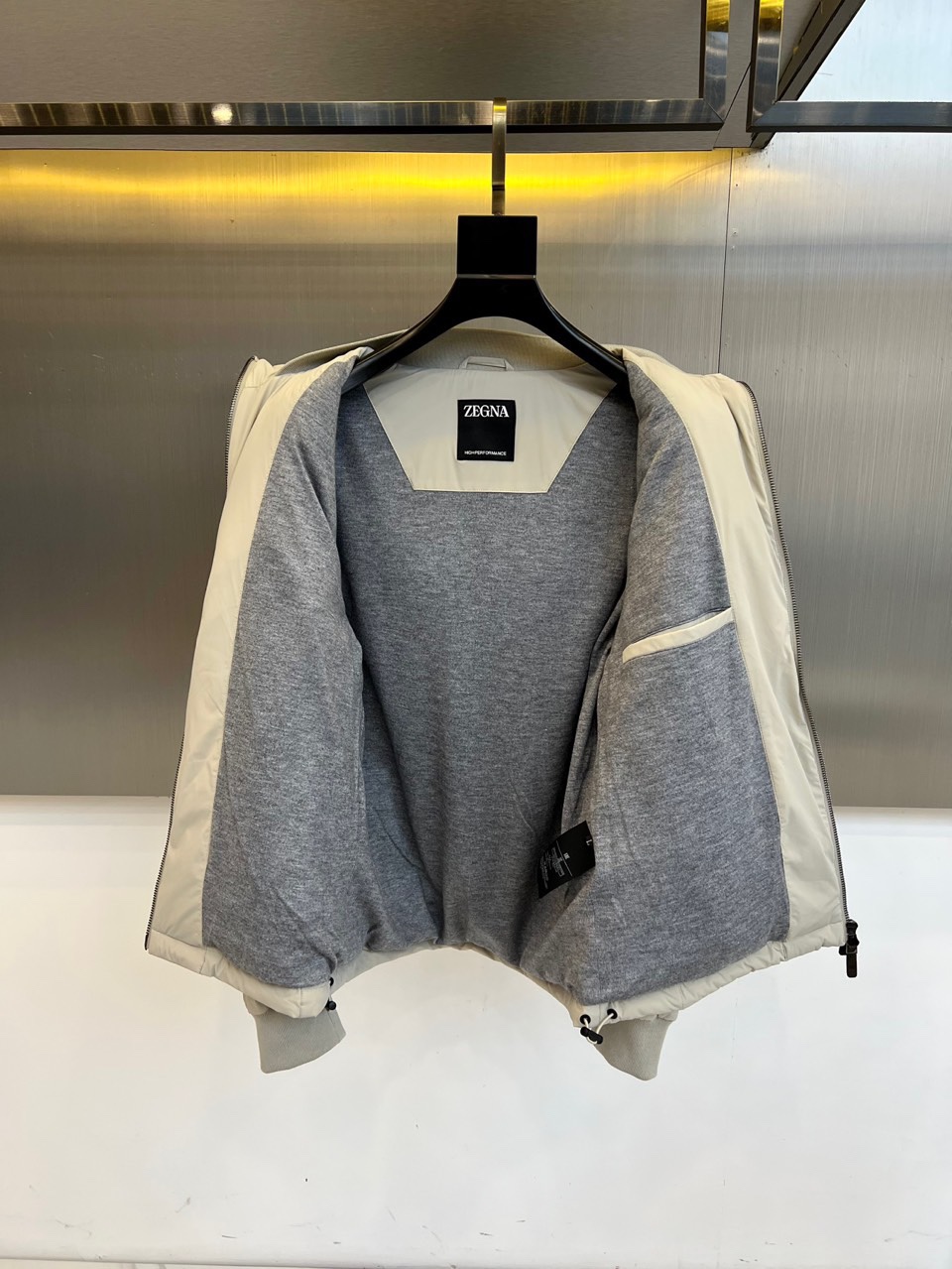 Zegna杰尼亚、2025秋冬新品羽绒服以浅灰质感演绎现代都市美学。这款连帽羽绒服采用极简立体剪裁，前襟