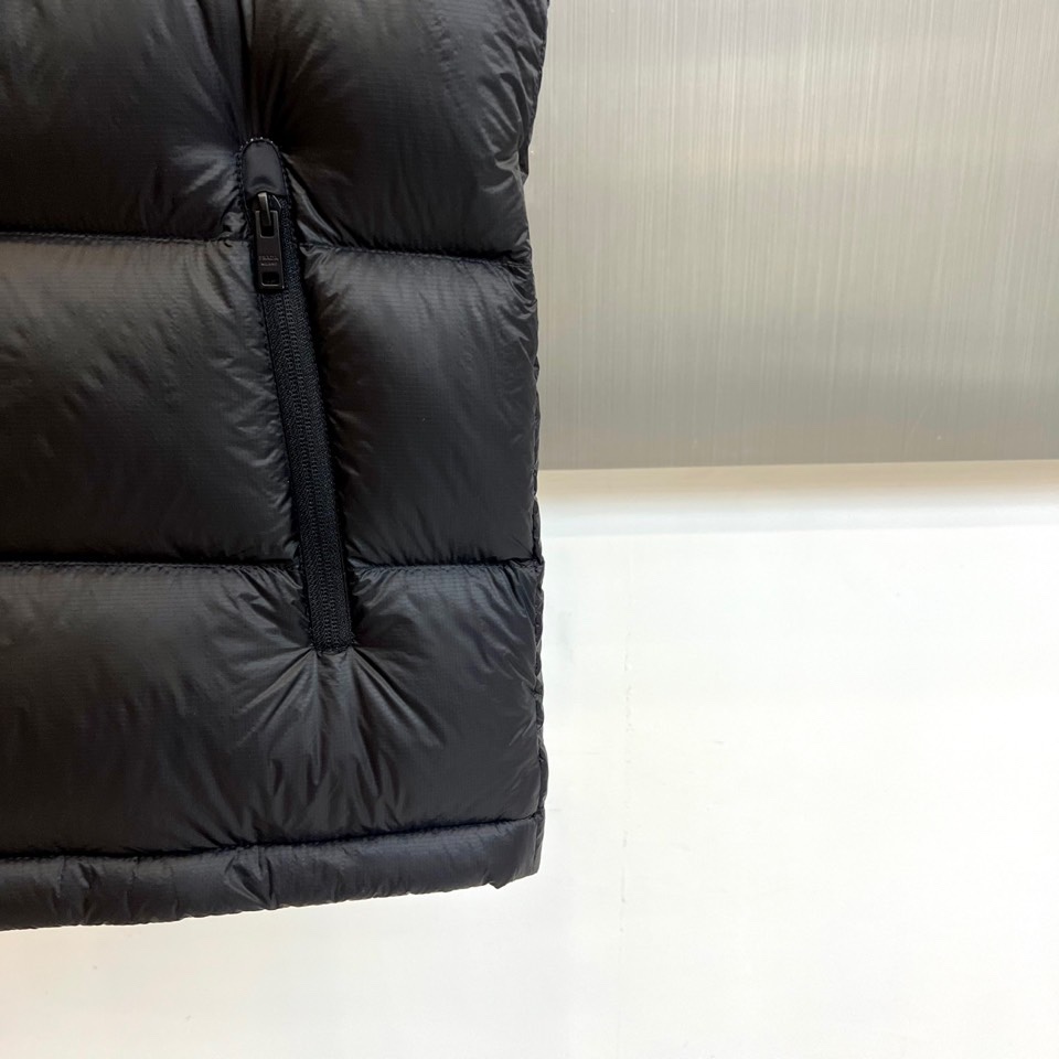 Prad普拉达、2025秋冬新品黑色羽绒马甲以简约设计诠释现代奢华。立领造型搭配顺滑拉链开合，勾勒出利落