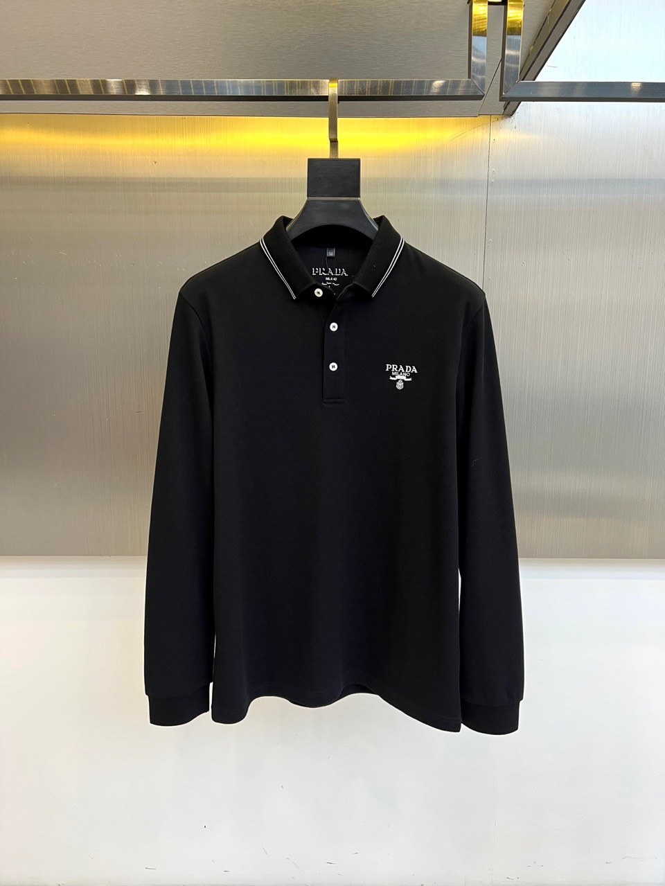 Prad普拉达、2025秋冬新品长袖Polo衫，经典翻领设计缀以黑蓝相间条纹边饰，领口下三颗米白色纽扣延