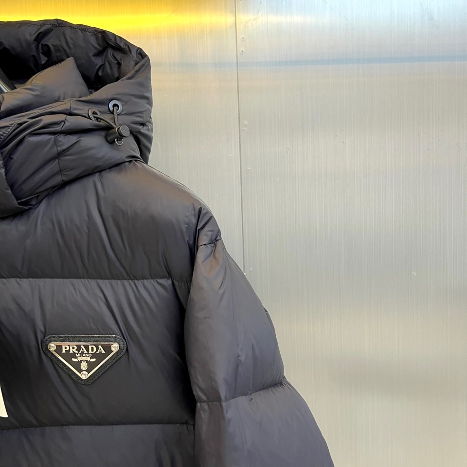 Prad普拉达、2025秋冬新品，黑色羽绒服诠释简约奢华的冬日美学。款式采用流畅的过膝廓形，搭配连帽设计