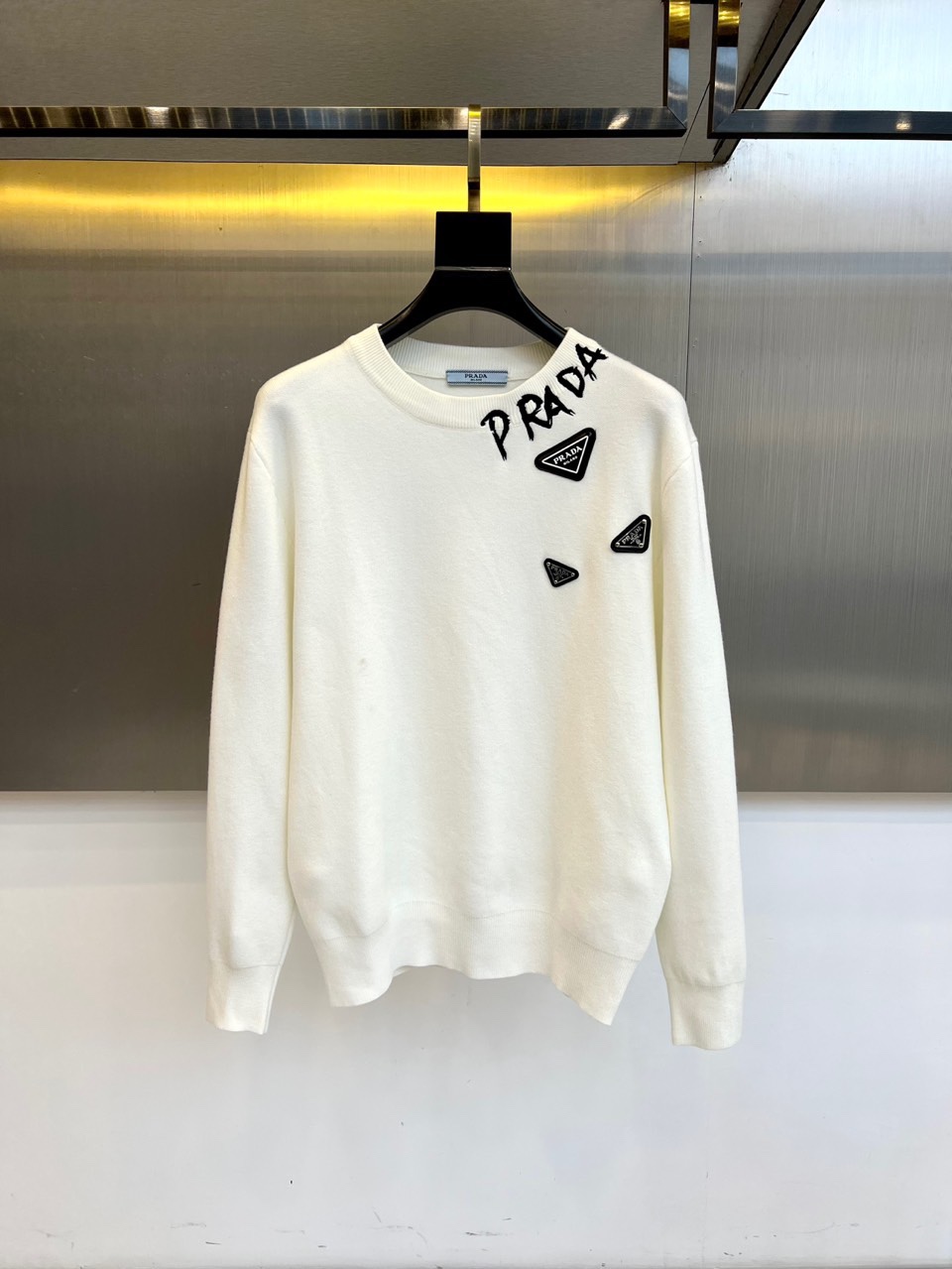 Prad普拉、2025秋冬新品白色针织毛衣，以极简主义美学诠释当代优雅。这款毛衣采用经典圆领设计，左胸位