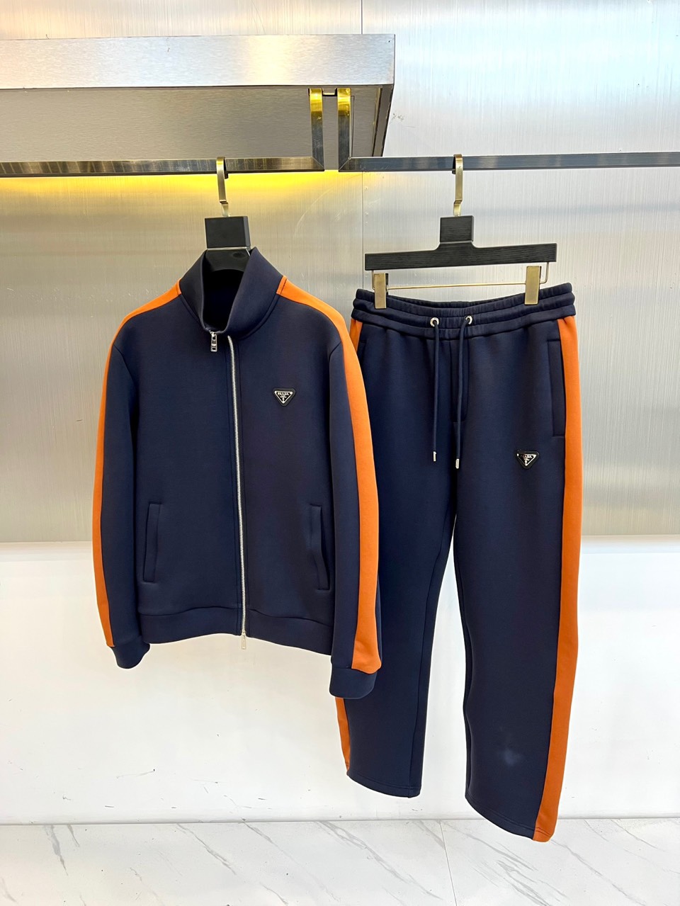 Prad普拉、2025秋冬运动系列。高密弹力面料构筑立体剪裁套装，橙棕条纹如赛道轨迹贯穿袖管与裤线。金属
