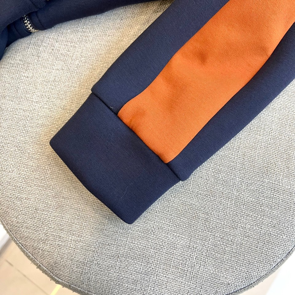 Prad普拉、2025秋冬运动系列。高密弹力面料构筑立体剪裁套装，橙棕条纹如赛道轨迹贯穿袖管与裤线。金属