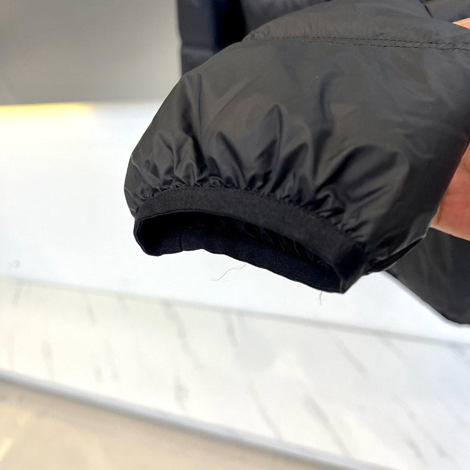 Mon蒙口（纯鹅绒）、2025秋冬新款羽绒服，以经典黑色演绎都市户外美学。这款连帽羽绒服采用横向绗缝工艺