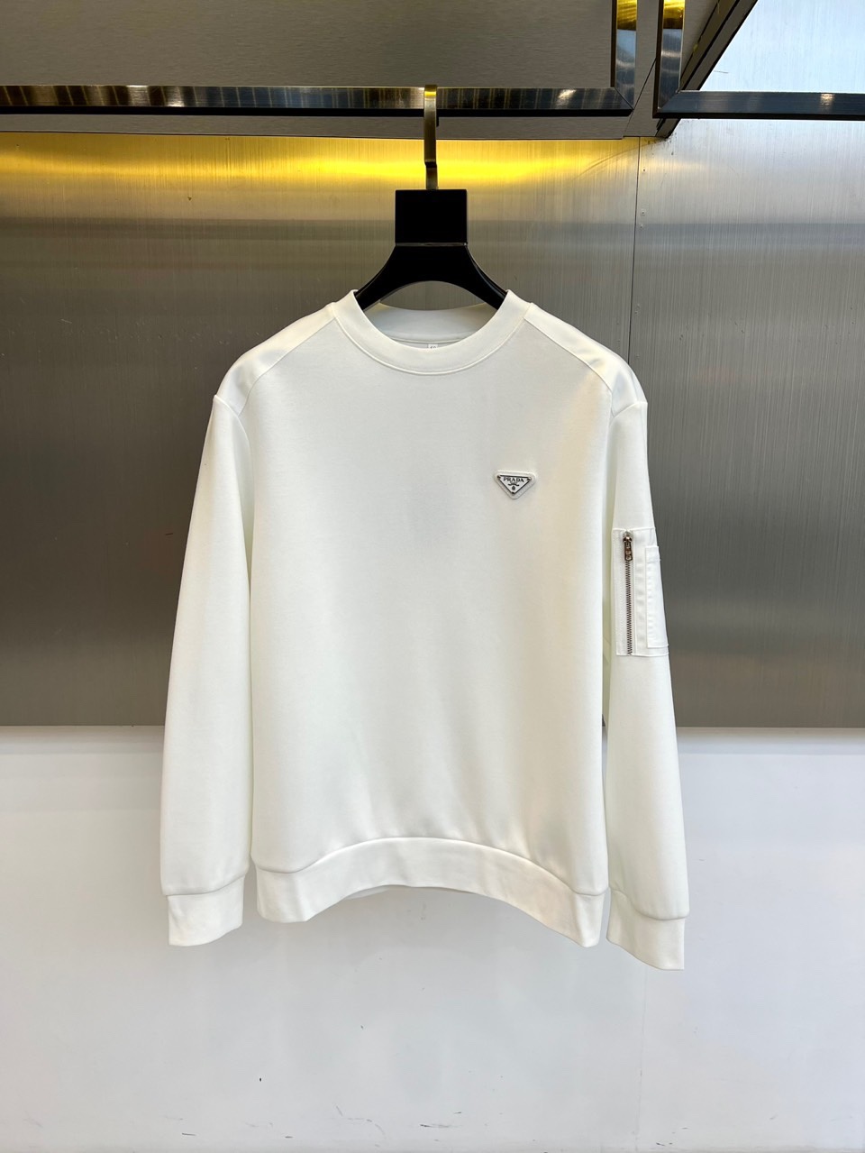 NO:681050,Prad, new products for autumn and winter | PRADA minimalist sweatshirt. This round-neck sweatshirt adopts a slightly wide version design, and the left chest is embellished with the brand's iconic triangular metal logo, which is polished to show a three-dimensional luster. The left arm is innovatively integrated into a hidden zipper pocket, which combines practical functions with avant-garde aesthetics. The fabric is made of worsted cotton, which is brushed to enhance a soft and skin-friendly touch. The ribbed cuffs and hem ensure a long-lasting and crisp fit.  The pure white tone continues the brand's minimalist gene, and the metal logo and zipper details inject a sense of low-key luxury into the basic style. It can be worn alone with jeans for urban casual style, or with a suit jacket to create a mixed look. Through the balance of iconic elements and practical design, PRADA's design philosophy of integrating Italian craftsmanship with modern wearability is interpreted. 48-56 (model 173, 143 pounds, upper body size 50),, prada, prada, hoodie, sweatshirts, jeans, jackets &  coats, business suits,19860909Prad普拉、秋冬新品 | PRADA极简卫衣.这款圆领卫衣采用微阔版型设计,左胸点缀品牌标志性三角形金属徽标,以抛光工艺呈现立体光泽.左臂创新融入隐藏式拉链口袋,兼具实用功能与前卫美学.面料选用精纺棉质材质,通过磨毛处理提升柔软亲肤触感,罗纹袖口与下摆确保版型持久挺括. 纯白基调延续品牌极简主义基因,金属徽标与拉链细节为基础款注入低调奢华感.可单穿搭配牛仔裤演绎都市休闲风,或外搭西装外套打造混搭造型.通过标志性元素与实用设计的平衡,诠释PRADA将意式工艺与现代实穿性相融合的设计哲学.48-56（模特173,143斤上身50码）,,prada,prada,hoodie,sweatshirts,jeans,jackets & coats,business suit,,Men's clothing