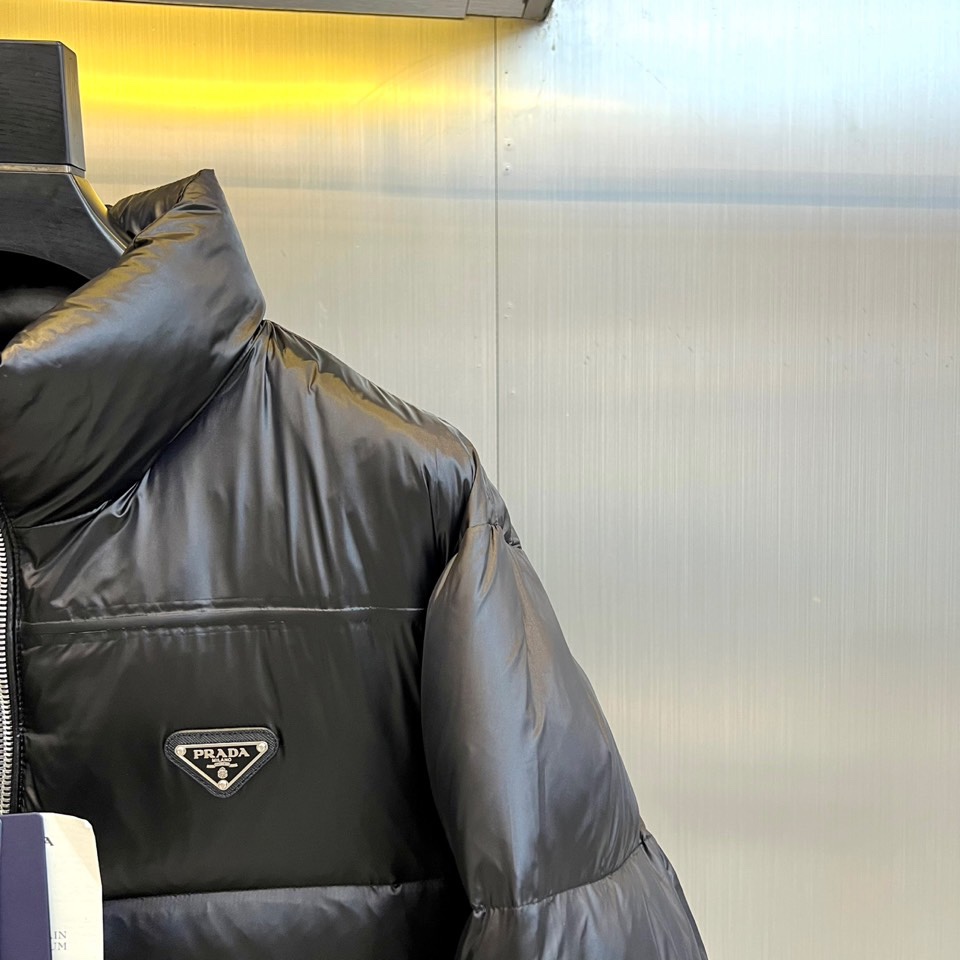 Prad普拉达、2025秋冬羽绒服，以极简美学重塑冬日防护。款式采用利落立领与流畅的箱型廓形，通过精准的