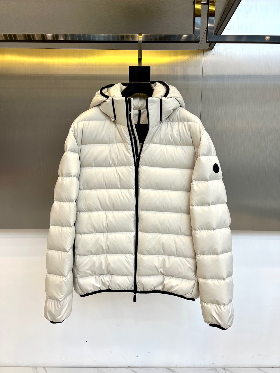 NO:681047,Mon, an autumn and winter down jacket, adopts a classic hooded silhouette. The fluffy and full quilting lines outline a three-dimensional architectural outline, effectively locking in warmth. The edges of the hood are decorated with black lines, which cleverly echo the long black zipper running through the front, injecting neat details into the pure tone. The brand's circular logo on the cuffs is low-key, highlighting extraordinary quality.  Its style is the perfect balance between urban functionality and daily relaxation. The off-white color tone is soft and versatile, giving the overall shape a high-end and clean visual experience. The crisp version does not appear bloated, whether it is paired with slim trousers to create a smart image, or integrated into casual wear, it can easily enhance the overall texture. The core filling is 90 high-quality pure  Goose down ensures extreme lightness while providing strong warmth and cold protection performance. This down jacket is not only a reliable equipment to deal with the cold winter, but also a key item to create a simple, warm and fashionable winter style. Sizes 1-5 (model is 173,143 pounds, upper body size 2),,Moncler,down  jacket,hats,19860909Mon蒙口、秋冬羽绒服,款式采用经典的连帽廓形,蓬松饱满的绗缝线条勾勒出立体的建筑感轮廓,有效锁住温暖.连帽边缘饰有黑色线条,与贯穿正面的黑色长拉链形成巧妙呼应,于纯净色调中注入利落细节.袖口的品牌圆形标识低调彰显非凡品质. 其风格是都市机能与日常松弛感的完美平衡.米白色调温柔百搭,赋予整体造型高级而干净的视觉感受.挺括的版型不显臃肿,无论是搭配修身长裤打造干练形象,还是融入休闲穿搭,都能轻松提升整体质感.核心填充90高品质纯鹅绒,确保在极致轻盈的同时提供强劲的保暖御寒性能.这件羽绒服不仅是应对寒冬的可靠装备,更是塑造冬日简约、温暖与时尚感并存风格的关键单品.1-5码（模特173,143斤上身2码）,,Moncler,down jacket,hats,,Men's clothing