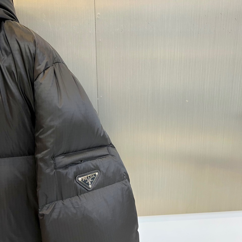 Prad普拉达、2025秋冬黑色羽绒服，以标志性设计语言重塑冬日温暖。款式采用宽松休闲的连帽廓形，帽檐配