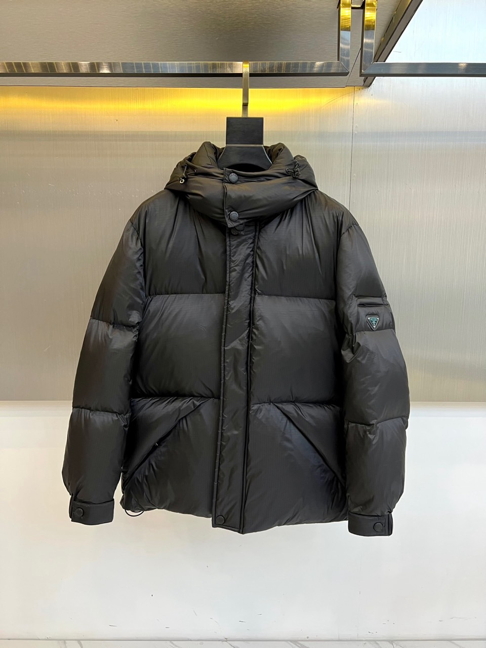 Prad普拉达、2025秋冬新品黑色羽绒服，以经典黑色重塑都市冬日美学。款式采用简约连帽设计，帽部点缀实