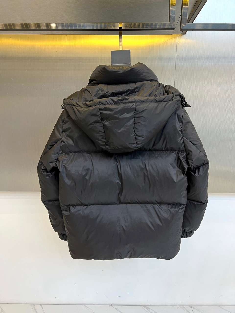 Prad普拉达、2025秋冬新品黑色羽绒服，以经典黑色重塑都市冬日美学。款式采用简约连帽设计，帽部点缀实