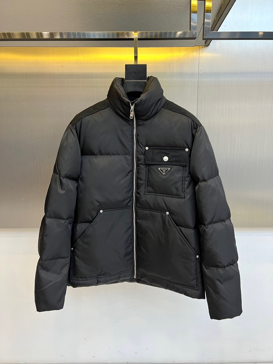 Prad普拉达、2025秋冬新品羽绒服，以纯黑色调演绎现代极简美学。款式采用利落立领设计，搭配银色拉链开