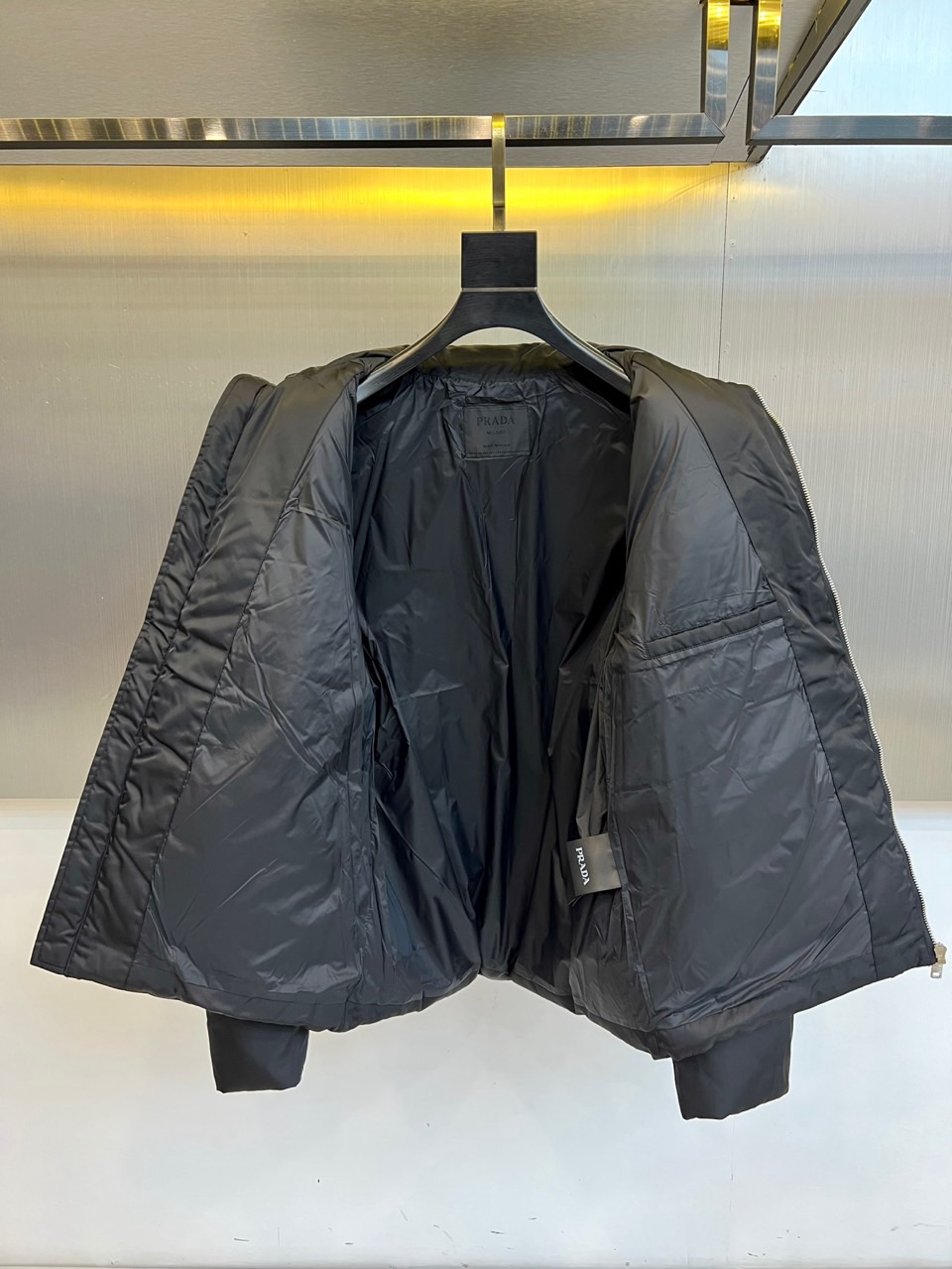 Prad普拉达、2025秋冬新品羽绒服，以纯黑色调演绎现代极简美学。款式采用利落立领设计，搭配银色拉链开