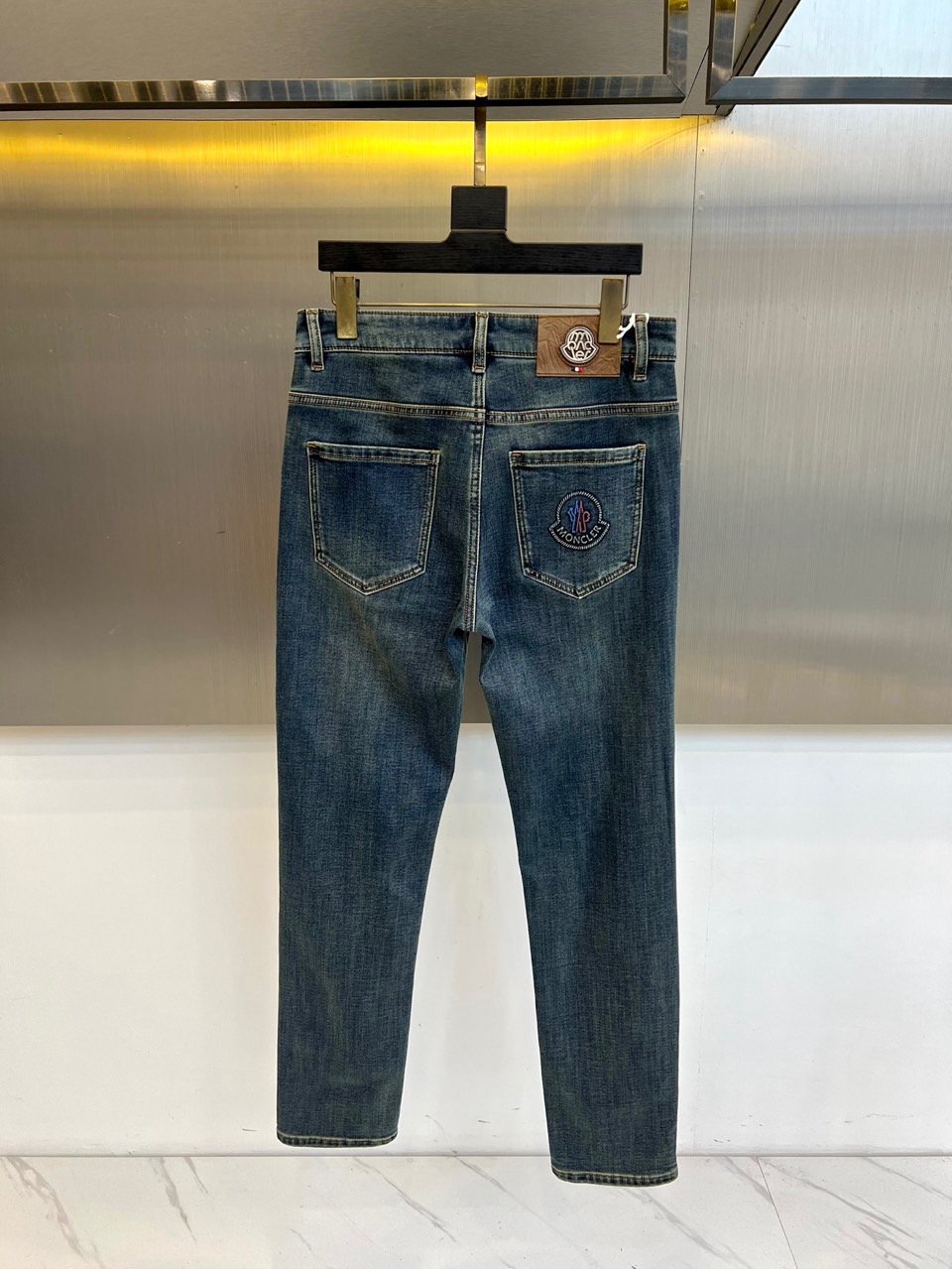 Mon蒙口、2025秋冬新品深蓝色牛仔裤以经典直筒版型演绎现代休闲美学。后袋饰以品牌标志性刺绣徽章，细腻