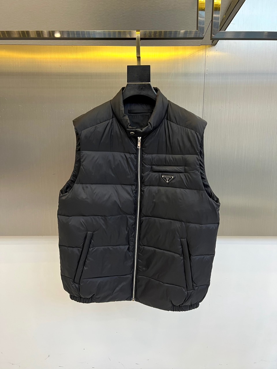 Prad普拉达、2025秋冬新品羽绒马甲以极简美学诠释实用主义时尚。这款黑色马甲采用经典无袖设计，通过精