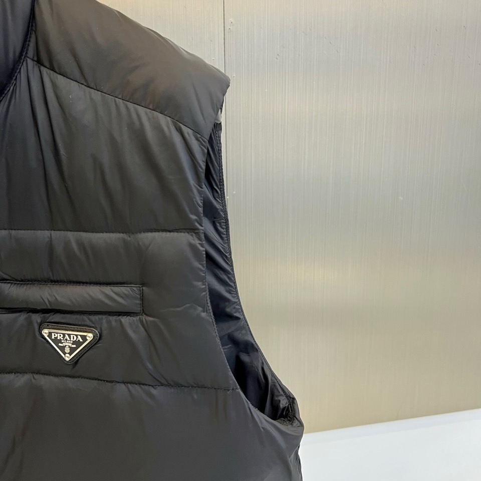 Prad普拉达、2025秋冬新品羽绒马甲以极简美学诠释实用主义时尚。这款黑色马甲采用经典无袖设计，通过精