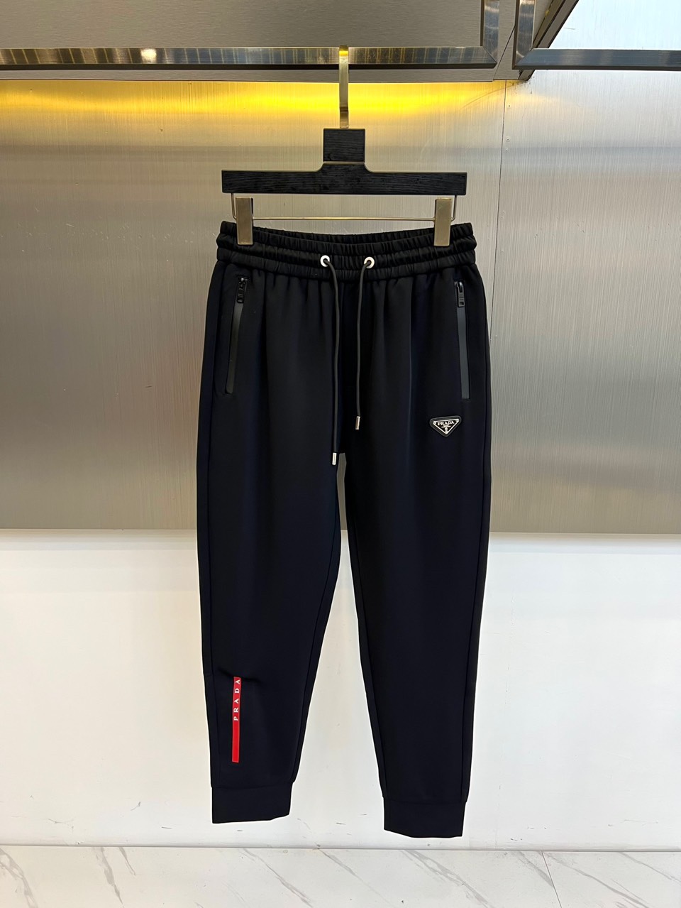 NO:685902,Prad, the new men's casual pants for autumn and winter 2025, are designed with an elastic waistband and an adjustable drawstring design. The diagonal pockets on both sides are integrated with invisible zipper details. The left trouser leg is decorated with the brand's iconic red triangle logo, and the knees are three-dimensionally cut to reserve room for movement. The fabric is made of high-tech blended materials, which are specially processed to present a delicate texture, with both breathability and anti-wrinkle performance. Its design combines pragmatism with Italian craftsmanship.  It can be paired with a sweater to create a business casual style, or it can be paired with sports shoes for a fun mix and match. From daily work to weekend trips, these trousers are designed with humanized details and iconic badges, becoming a carrier that connects urban life and fashion attitude, interpreting Prada’s in-depth exploration of modern dress aesthetics. 48-56 (model 173, 143 pounds, upper body size 50),, prada, prada, sneakers,19860909Prad普拉、2025秋冬新品男士休闲裤,款式采用弹性腰头搭配可调节抽绳设计,两侧斜插口袋融入隐形拉链细节,左裤腿饰有品牌标志性红色三角徽标,膝部采用立体剪裁预留活动空间.面料选用高科技混纺材质,通过特殊处理呈现细腻肌理感,兼具透气性与抗皱性能.其设计将实用主义与意式工艺相融合,可搭配针织衫打造商务休闲风范,亦可与运动鞋碰撞出混搭趣味.从日常工作到周末出行,这款长裤以人性化细节与标志性徽章设计,成为连接都市生活与时尚态度的载体,诠释Prada对现代着装美学的深度探索.48-56（模特173,143斤上身50码）,,prada,prada,sneakers,,Men's clothing