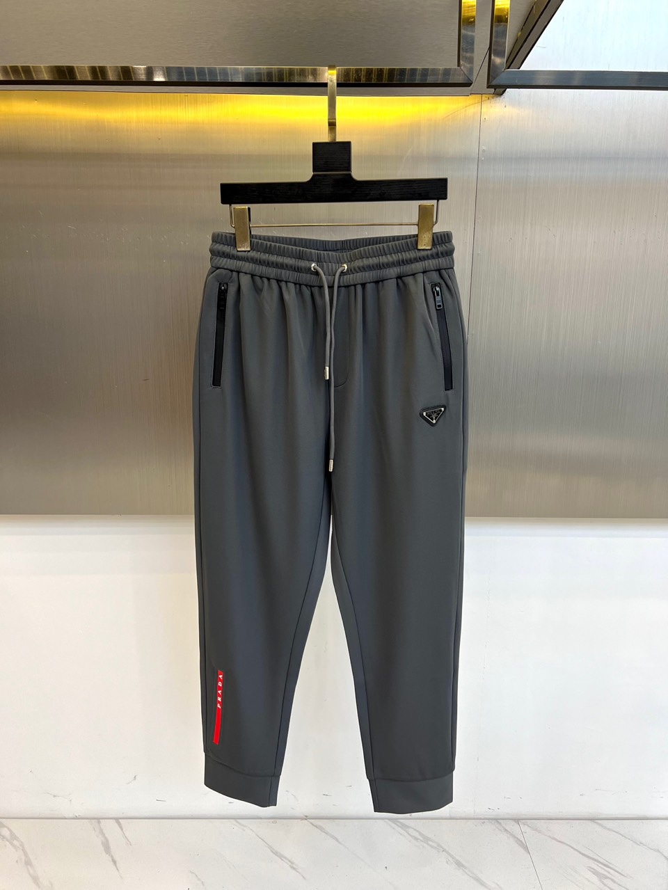 NO:684318,Prad, the new men's casual pants for autumn and winter 2025, are designed with an elastic waistband and an adjustable drawstring design. The diagonal pockets on both sides are integrated with invisible zipper details. The left trouser leg is decorated with the brand's iconic red triangle logo, and the knees are three-dimensionally cut to reserve room for movement. The fabric is made of high-tech blended materials, which are specially processed to present a delicate texture, with both breathability and anti-wrinkle performance. Its design combines pragmatism with Italian craftsmanship.  It can be paired with a sweater to create a business casual style, or it can be paired with sports shoes for a fun mix and match. From daily work to weekend trips, these trousers are designed with humanized details and iconic badges, becoming a carrier that connects urban life and fashion attitude, interpreting Prada’s in-depth exploration of modern dress aesthetics. 48-56 (model 173, 143 pounds, upper body size 50),, prada, prada, sneakers,19860909Prad普拉、2025秋冬新品男士休闲裤,款式采用弹性腰头搭配可调节抽绳设计,两侧斜插口袋融入隐形拉链细节,左裤腿饰有品牌标志性红色三角徽标,膝部采用立体剪裁预留活动空间.面料选用高科技混纺材质,通过特殊处理呈现细腻肌理感,兼具透气性与抗皱性能.其设计将实用主义与意式工艺相融合,可搭配针织衫打造商务休闲风范,亦可与运动鞋碰撞出混搭趣味.从日常工作到周末出行,这款长裤以人性化细节与标志性徽章设计,成为连接都市生活与时尚态度的载体,诠释Prada对现代着装美学的深度探索.48-56（模特173,143斤上身50码）,,prada,prada,sneakers,,Men's clothing