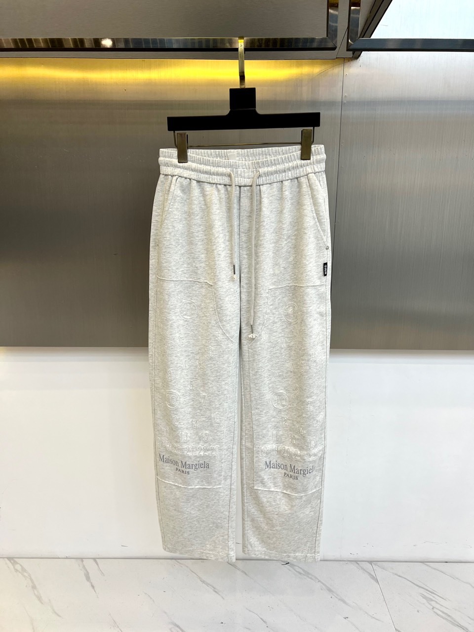 NO:684330,[Maison Margiela | Logo printed casual trousers] Deconstructed drawstring waistband｜All-over brand logo printing｜Diagonal pockets Deconstructed drawstring waistband Light gray fabric with same-color drawstrings, the waistband structure drapes naturally, continuing the brand's consistent deconstruction language, combining comfort and design. Brand logo printed all over the pants 'Maison Margiela' printed all over the body  PARIS' words and the brand's iconic digital pattern form a strong visual symbol, highlighting the brand's unique identity expression. Practical slant pockets Keep simple slant pockets on both sides, taking into account daily practicality, without destroying the visual coherence and flow of the overall printing. Drape and loose tailoring adopts a loose straight version, and the fabric hangs naturally. Through the echo of printing and tailoring, it creates a lazy and artistic daily look.  Suitable for matching with simple tops, highlighting the strong brand imprint and design style of the trousers themselves, creating a low-key and avant-garde daily wear. M-3XL (please state height, weight and waistline when placing an order),,19860909【Maison Margiela | 标志印花休闲长裤】 解构抽绳腰头｜满印品牌标识｜斜插口袋 解构感抽绳腰头 浅灰面料搭配同色抽绳,腰头结构自然垂坠,延续品牌一贯的解构语言,兼具舒适与设计感. 满印品牌标识 裤身满幅印制“Maison Margiela PARIS”字样及品牌标识性数字图案,形成强烈的视觉符号,突出品牌独特的身份表达. 实用斜插口袋 两侧保留简洁斜插口袋,兼顾日常实用性,不破坏整体印花视觉的连贯性与流动感. 垂坠宽松剪裁 采用宽松直筒版型,面料自然垂顺,通过印花与剪裁的呼应,营造出慵懒而富有艺术感的日常造型. 适合搭配简约上衣,突出裤装本身强烈的品牌印记与设计风格,打造低调前卫的日常穿搭.M-3XL（下单请报、身高体重腰围）,,,Men's clothing
