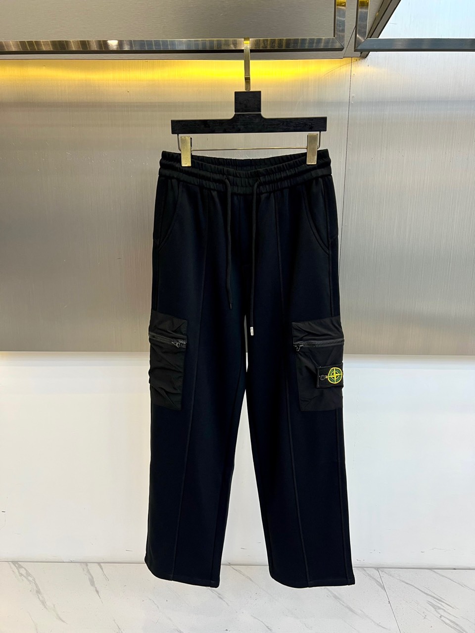 NO:684303,[Stone Island｜Functional workwear casual pants] Elastic drawstring waistband｜Large-capacity zipper pockets on both sides｜Classic compass mark Elastic functional fabric Made of black elastic fabric, taking into account daily comfort and freedom of movement, suitable for wearing in many scenes. Large-capacity zipper bags on both sides Three-dimensional large-capacity zipper pockets on both sides of the thighs enhance practical storage functions, and the neat lines and zipper design enhance the tough workwear style. Classic compass mark embellishment Stone on the pocket  Island's iconic yellow compass logo embroidery becomes a highlight detail on the black pants, low-key highlighting the brand recognition. The elasticated drawstring waistband has a built-in elastic waistband with a drawstring of the same color, which can be flexibly adjusted to provide a comfortable fit while maintaining a simple silhouette of the waist. It combines practical functional details with the classic brand logo, suitable for daily commuting, urban exploration and other occasions, interpreting a low-key yet recognizable functional aesthetic. M-3XL (please state your height and weight when placing an order),19860909【Stone Island｜机能工装休闲裤】 松紧抽绳腰头｜双侧大容量拉链袋｜经典罗盘标 弹力机能面料 采用黑色弹力面料,兼顾日常舒适度与活动自由度,适合多场景穿着. 双侧大容量拉链袋 大腿两侧搭载立体大容量拉链口袋,增强实用储物功能,利落线条与拉链设计强化硬朗工装风格. 经典罗盘标点缀 口袋上饰有 Stone Island 标志性黄色罗盘标刺绣,成为黑色裤身上的高亮细节,低调彰显品牌辨识度. 松紧抽绳腰头 内置弹性腰围搭配同色抽绳,可灵活调节松紧,在提供舒适贴合感的同时保持腰部简洁轮廓. 以实用机能细节与经典品牌标识结合,适配日常通勤、都市探索等场合,诠释低调而具辨识度的机能美学.M-3XL（下单请报身高体重腰围）,,,Men's clothing