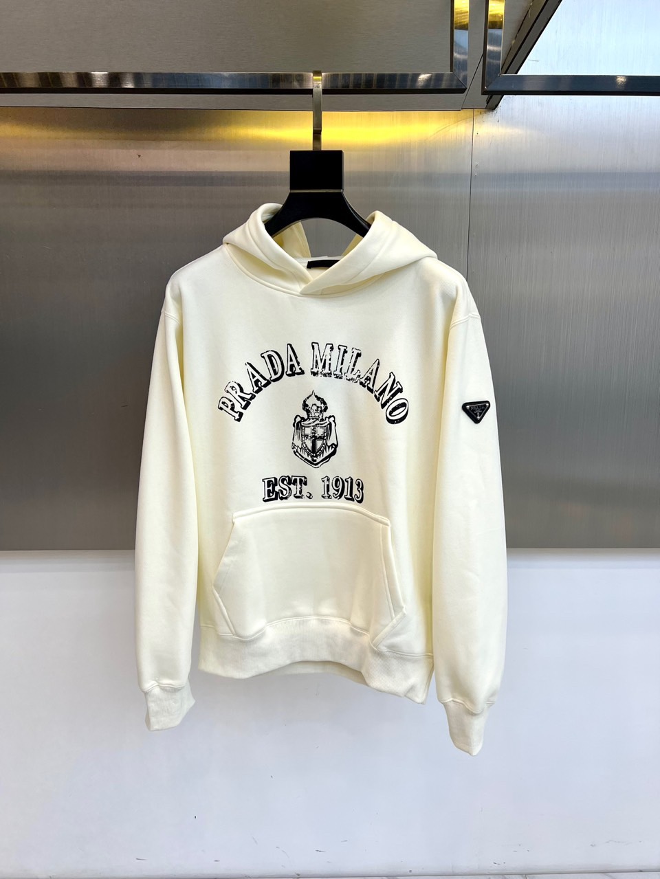 NO:684316,Prada, the new Prada hooded sweatshirt for autumn and winter 2025, uses off-white thick fabric to present a classic and simple urban casual style. The 'PRADA MILANO' black brand logo and retro badge pattern are eye-catchingly embellished on the chest, with 'EST.  The words 1913' emphasize the timeless style of the brand's century-old heritage. The hooded design and loose tailoring create a lazy and comfortable daily atmosphere. The left cuff is decorated with a classic triangular metal logo, highlighting the brand's genes in every detail. The overall design cleverly blends the casual sense with the language of high fashion, both  Practical and recognizable, it is an ideal item for creating a low-key and textured daily look in autumn and winter. S-4XL (model 173-140 pounds upper body size M),, prada, prada, hoodie, sweatshirts, hats,19860909普拉达、2025秋冬新品Prada连帽卫衣,以米白色厚实面料呈现经典简约的都市休闲风格.胸前醒目点缀“PRADA MILANO”黑色品牌标识及复古徽章图案,搭配“EST. 1913”字样,强调品牌百年传承的隽永格调.连帽设计与宽松剪裁营造出慵懒舒适的日常氛围,左袖口饰有经典三角金属标识,于细节处彰显品牌基因.整体将休闲感与高级时装语言巧妙融合,兼具实穿度与辨识度,是秋冬打造低调而有质感的日常造型的理想单品.S-4XL（模特173-140斤上身M码）,,prada,prada,hoodie,sweatshirts,hats,,Men's clothing