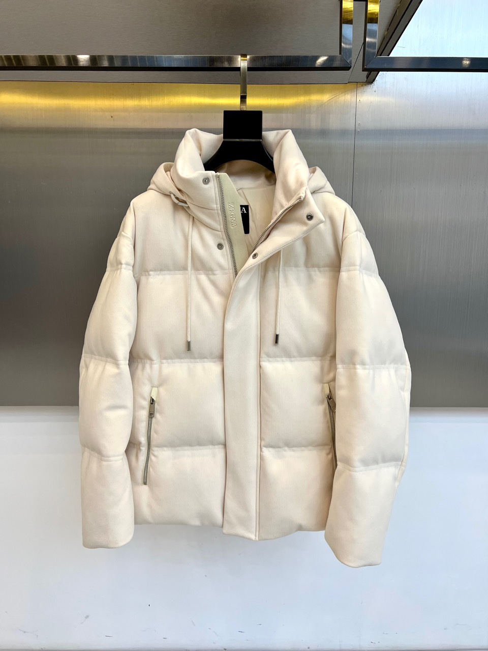 NO:703194,ZEGNA Zegna's new autumn and winter men's down jacket features a hooded design with an adjustable drawstring. The placket is equipped with a smooth metal zipper opening and closing system, and the left breast pocket is embellished with a brand logo badge. The body of the jacket is formed with a three-dimensional checkered texture through precise architectural quilting technology to ensure the even distribution of high-quality down. The diagonal pockets on both sides are both practical and smooth. The fabric is strictly made of polyester fiber, and the exquisite quality of Made in China is reflected in the delicate stitching process and precise tailoring.  Its design combines sharp Italian tailoring with outdoor functionality, and its loose fit fits a variety of body shapes. It can be paired with business casual pants to show urban elegance, or it can be paired with jeans for a fun mix and match. From business commuting to weekend trips, this down jacket combines simple quilted lines with  Practical details have become a winter model that connects high-end craftsmanship with daily practicality, interpreting ZEGNA's dual pursuit of material craftsmanship and practical aesthetics. 48-56 (model weighs 173,143 pounds, upper body size 50),,zegna,jeans,down  jacket,hats,19860909ZEGNA杰尼亚、秋冬新品男士羽绒服,款式采用连帽设计搭配可调节抽绳,门襟配置顺滑金属拉链开合系统,左侧胸袋点缀品牌标识徽章.衣身通过精准的建筑感绗缝工艺形成立体方格纹理,确保高品质羽绒均匀分布,两侧斜插口袋兼顾实用功能与流畅线条.面料严格选用聚酯纤维材质,中国制造的精工品质体现在细腻的缝线工艺与精准剪裁. 其设计将意式利落剪裁与户外功能性相融合,宽松版型适配多种身形需求,可搭配商务休闲裤展现都市优雅,亦可与牛仔裤碰撞出混搭趣味.从商务通勤到周末出行,这款羽绒服以简约的绗缝线条与实用细节,成为连接高端匠心与日常实穿性的冬季典范,诠释ZEGNA对材质工艺与实用美学的双重追求.48-56（模特173,143斤上身50码）,,zegna,jeans,down jacket,hats,,Men's clothing