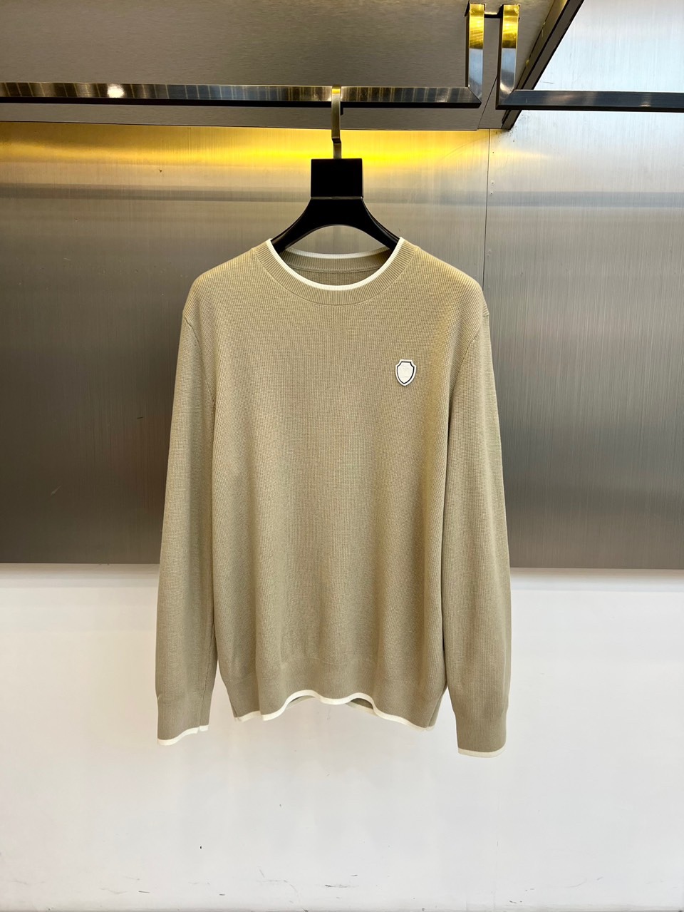 NO:703197,Brunello cucinelli-BC, a new knitted sweater for autumn and winter. The round neck design is matched with white trimming on the collar and hem. The shield logo on the left chest is embroidered in the same color to present a low-key texture. It uses a golden ratio of 72.6 wool and 5.8 cashmere. The wool gives the fabric a delicate bone texture, and the cashmere is injected with a soft and waxy touch like a cloud. It also contains 21.6 anti-pilling fibers to improve durability.  10-needle dense weaving technology creates a uniform slub texture, and ribbed edges ensure a long-lasting and crisp silhouette. The main tone of khaki echoes autumn earth tones, and the white trim outlines a simple outline. It can be paired with chinos for business casual or jeans for everyday elegance.  Ya. From the material ratio to the trim details, it interprets Brunello Cucinelli's 'quiet luxury' philosophy of integrating the spirit of Italian craftsmanship into daily wear. 48-56 (model 173, 143 pounds, upper body size 50),, brunello  cucinelli,jeans,gold,19860909Brunello cucinelli-BC,秋冬新品针织衫.圆领设计搭配领口与下摆的白色镶边工艺,左胸盾形徽标以同色系刺绣呈现低调质感.采用72.6羊毛与5.8羊绒的黄金配比,羊毛赋予织物细腻骨感,羊绒注入云朵般软糯触感,另含21.6抗起球纤维提升耐久度. 10针密织技术形成均匀竹节纹理,罗纹收边确保版型持久挺括.卡其主调呼应秋日大地色系,白色镶边勾勒简约轮廓,既可搭配斜纹裤演绎商务休闲,亦可配合牛仔裤打造日常优雅.从材质配比到镶边细节,诠释布鲁奈罗·库奇内利将意大利手工精神融入日常穿着的「安静奢华」哲学.48-56（模特173,143斤上身50码）,,brunello cucinelli,jeans,gold,,Men's clothing