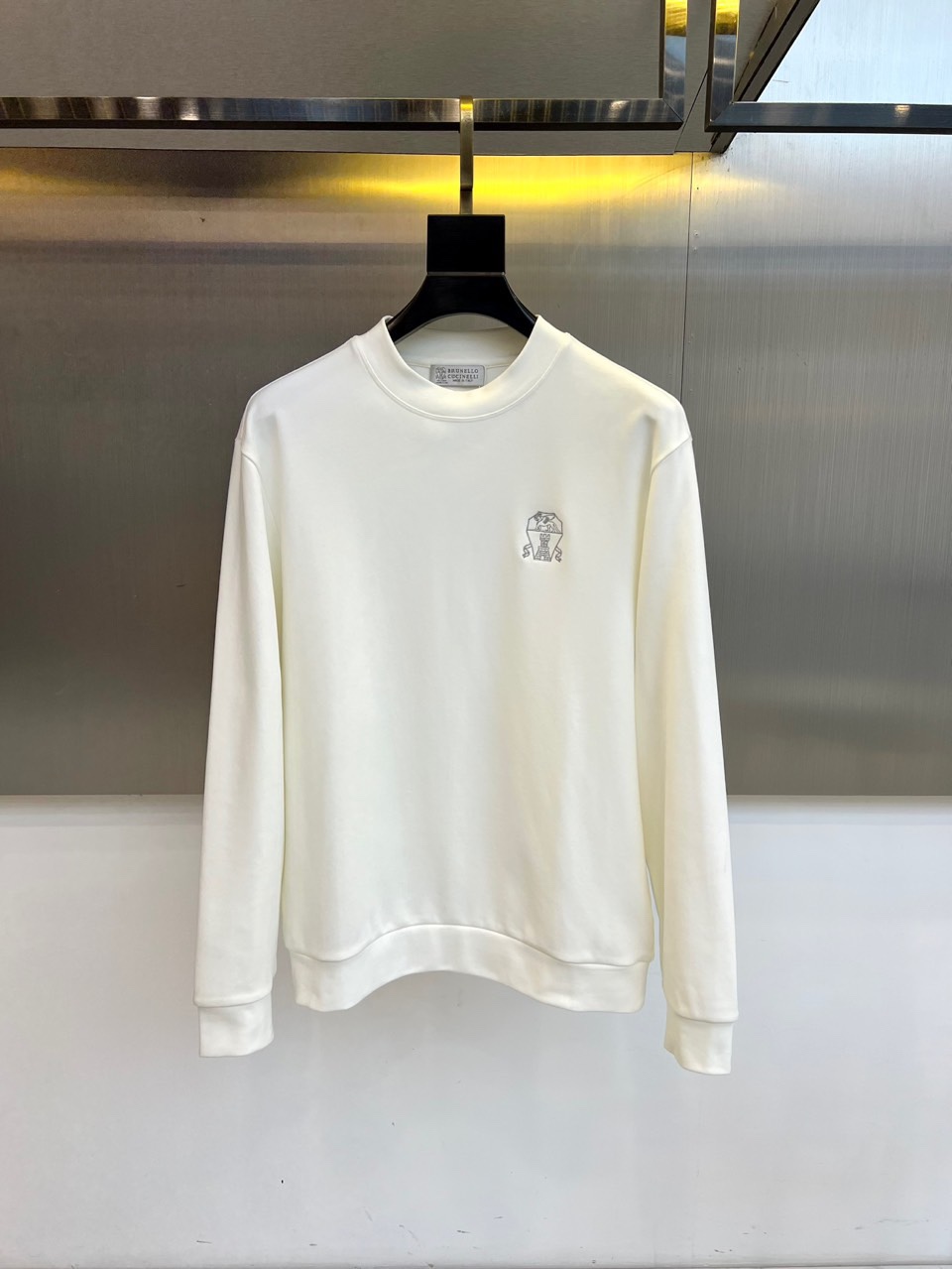 NO:703203,BRUNELLO CUCINELLI  The new autumn and winter sweatshirt interprets low-key luxury with a simple design. The round-neck style uses double-layer fabric hemming technology to ensure that the neckline does not deform for a long time. The left chest is decorated with the brand's iconic embroidered badge, and the same-color silk thread is used to outline a delicate three-dimensional pattern, showing Italian tailoring aesthetics. The body is made of the brand's exclusive cotton blend fabric, which has been specially washed to present a soft and skin-friendly texture. The slightly loose version has precise control of the armhole and length ratio to ensure freedom of movement.  The hem and cuffs are trimmed with high-density ribbing, and the inner seams are brushed to avoid friction. This sweatshirt can be paired with casual trousers to create a daily look, or it can be worn under a jacket. Its pure white tone and exquisite detail design perfectly interpret the brand's philosophy of sublimating daily clothing into luxury items. 48-56 (model is 173, 143 pounds, upper body size 50), brunello  cucinelli,hoodie,sweatshirts,jackets & coats,19860909BRUNELLO CUCINELLI 秋冬新品卫衣,以简约设计诠释低调奢华.圆领款式采用双层面料包边工艺,确保领口持久不变形.左胸处装饰品牌标志性刺绣徽章,以同色丝线勾勒出细腻的立体图案,展现意式精裁美学.衣身采用品牌专属的棉质混纺面料,经过特殊水洗处理呈现柔软亲肤的肌理感.微宽松版型在袖笼与衣长比例上精准把控,既保证活动自由度又不失利落轮廓.下摆与袖口采用高密度罗纹收边,内侧缝线均经过磨毛处理避免摩擦感.这款卫衣可搭配休闲长裤打造日常造型,亦可在外套内展现层次穿搭,其纯净白色调与精致细节设计,完美演绎了品牌将日常服饰升华为奢华单品的哲学理念.48-56（模特173,143斤上身50码）,,brunello cucinelli,hoodie,sweatshirts,jackets & coats,,Men's clothing