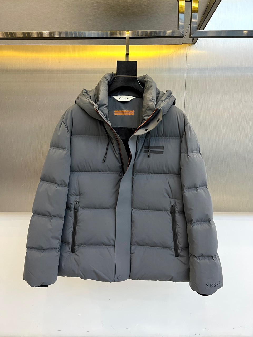 NO:703213,Zegn Ermenegildo Zegna's new autumn and winter down jacket interprets modern urban outdoor aesthetics with calm tones. The style adopts a hooded design, and the hood is equipped with an adjustable drawstring and a button windshield to enhance practical protection. The front is divided by horizontal quilting, taking into account the bulkiness and clean outline. The left chest is decorated with two dark stripes, and the lower side of the right sleeve is embellished with the brand logo. Both sides are equipped with zippered slant pockets for safe storage and smooth lines.  The fabric is made of high-density polyester fiber, which is windproof and waterproof, and is filled with high-quality down to ensure warmth and lightness. The details reflect Italian precision, such as the smooth zipper system and uniform quilting. The overall design combines Alpine functional genes with urban simplicity, and the horizontal quilting and armbands become low-key identity marks.  This down jacket can not only cope with urban autumn and winter commuting, but also accompany outdoor trips on weekends. It perfectly interprets Zegna's design philosophy of integrating high-performance materials and Italian elegance. The product is marked as produced in China and strictly follows the brand's process standards to achieve seamless switching from mountain-inspired urban scenes. 48-56 (model is 173,143 pounds, upper body size 50),,zegna,down jacket,hats,19860909Zegn杰尼亚、秋冬新品羽绒服,以沉稳色调诠释现代都市户外美学.款式采用连帽设计,帽部配备可调节抽绳与纽扣挡风片,增强实用防护性.正面运用横向绗缝分割,兼顾蓬松度与利落轮廓.左胸饰有两道深色条纹装饰,右袖下侧点缀品牌标识.两侧配备带拉链的斜插口袋,兼顾安全储物与流畅线条. 面料采用高密度聚酯纤维,具备防风防水性能,内填充高品质羽绒确保温暖轻盈.细节处体现意式精工,如顺滑拉链系统与均匀绗缝.整体将阿尔卑斯功能基因与都市简约风格相融合,横向绗缝与袖标成为低调的身份印记. 这款羽绒服既能应对城市秋冬通勤,亦能陪伴周末户外出行,完美诠释杰尼亚融合高性能材质与意式优雅的设计哲学.产品标注产地为中国,严格遵循品牌工艺标准,实现从高山灵感都市场景的无缝切换.48-56（模特173,143斤上身50码）,,zegna,down jacket,hats,,Men's clothing