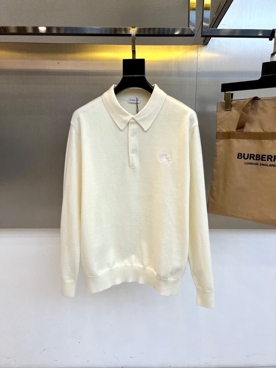 NO:711999,Burberry, the new men's knitted Polo shirt for autumn and winter 2025 interprets modern British style in warm off-white. This long-sleeved Polo shirt is made of cotton fabric to create a soft texture. It has a classic lapel design with three white buttons and the brand's iconic logo on the left chest.  Knight embroidered badge. The body adopts three-dimensional cutting technology, and the cuffs and hem are ribbed to keep the silhouette crisp. The lining is specially made of 70 wool and 30 cashmere blended materials, and the brand plaid details are integrated into the collar and back. Its design combines the casual feel of traditional Polo shirts with  The high-end texture of knitted items is perfectly integrated, and the off-white tone gives the autumn and winter style a warm atmosphere. From business casual occasions to weekend social gatherings, this Polo shirt can show the elegance of a modern gentleman with exquisite craftsmanship and low-key details. The label is clearly marked Portugal  Exquisitely crafted, it demonstrates the brand's persistent pursuit of quality and has become a classic item in the autumn and winter wardrobe that is both practical and brand-recognizable. 48-56 (model weighs 173,143 pounds, upper body size 50),,burberry,burberry,19860909Bur巴宝莉、2025秋冬新品男士针织Polo衫以温润米白诠释现代英伦风尚.这款长袖Polo衫采用棉质面料打造柔软肌理,经典翻领设计搭配三粒白色纽扣,左胸点缀品牌标志性骑士刺绣徽章.衣身采用立体剪裁工艺,袖口与下摆以罗纹收边保持廓形挺括,内衬特别采用70羊毛与30羊绒混纺材质,于领背处融入品牌格纹细节.其设计将传统Polo衫的休闲感与针织单品的高级质感完美融合,米白色调赋予秋冬造型温润气息.从商务休闲场合到周末社交聚会,这件Polo衫都能以考究工艺与低调细节展现现代绅士的儒雅气质.标签明确标注葡萄牙精工制作,彰显品牌对品质的执着追求,成为秋冬衣橱中兼具实穿性与品牌辨识度的经典单品.48-56（模特173,143斤上身50码）,,burberry,burberry,,Men's clothing