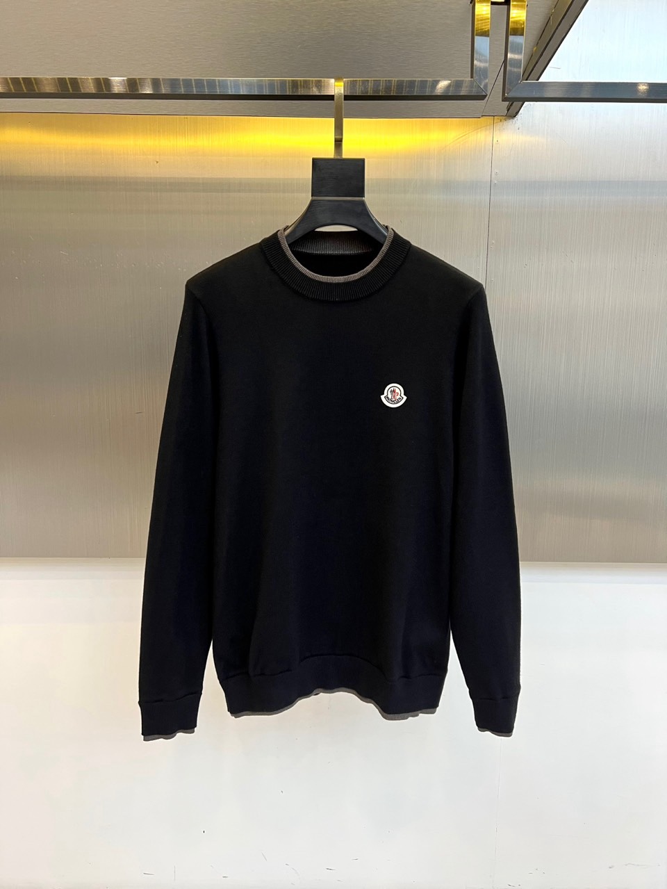 NO:712002,Mon, the 2025 autumn and winter new black sweater, interprets timeless elegance with a classic round neck design. The brand's iconic embossed badge is embellished on the left chest, and the three-dimensional outline is outlined with exquisite embroidery technology. The body is made of worsted merino wool and is woven with fine stitches  It has a uniform texture, and the hem and cuffs are integrated with dark gray contrasting ribbed edges to form a subtle layered transition. The fabric has been specially treated with anti-shrinkage to maintain a stiff shape while still having a soft touch like cashmere. The knitted structure with a moderate weight achieves a balance between warmth and breathability.  It can be paired with trousers of the same color to create a business casual style, or it can be combined with jeans for a mixed and matched charm. The badge details are made of washable embroidery thread, which will maintain its three-dimensional shape after repeated washing, and the contrasting ribs not only strengthen the outline but also inject modernity into the whole. This sweater shows Meng Mou's insistence on materials and craftsmanship with low-key details, and has become a must-have item in the autumn and winter wardrobe across all occasions. M-4XL (model weighs 173,143 pounds, upper body size L), Moncler, jeans,19860909Mon蒙口、2025秋冬新品黑色毛衫以经典圆领设计诠释永恒优雅.左胸处点缀品牌标志性浮雕徽章,以精湛刺绣工艺勾勒出立体轮廓.衣身采用精纺美利奴羊毛材质,细腻针脚织就均匀肌理,下摆与袖口融入深灰撞色罗纹收边,形成微妙层次过渡.面料经过特殊防缩处理,保持挺括版型的同时兼具羊绒般柔软触感,克重适中的针织结构实现保暖性与透气度的平衡. 可搭配同色系西裤塑造商务休闲风范,亦能与牛仔裤碰撞出混搭魅力.徽章细节采用耐洗绣线,经多次洗涤仍保持立体形态,撞色罗纹既强化轮廓又为整体注入现代感.这件毛衫以低调细节展现蒙口对材质与工艺的坚持,成为秋冬衣橱中跨越场合的必备单品.M-4XL（模特173,143斤上身L码）,,Moncler,jeans,,Men's clothing