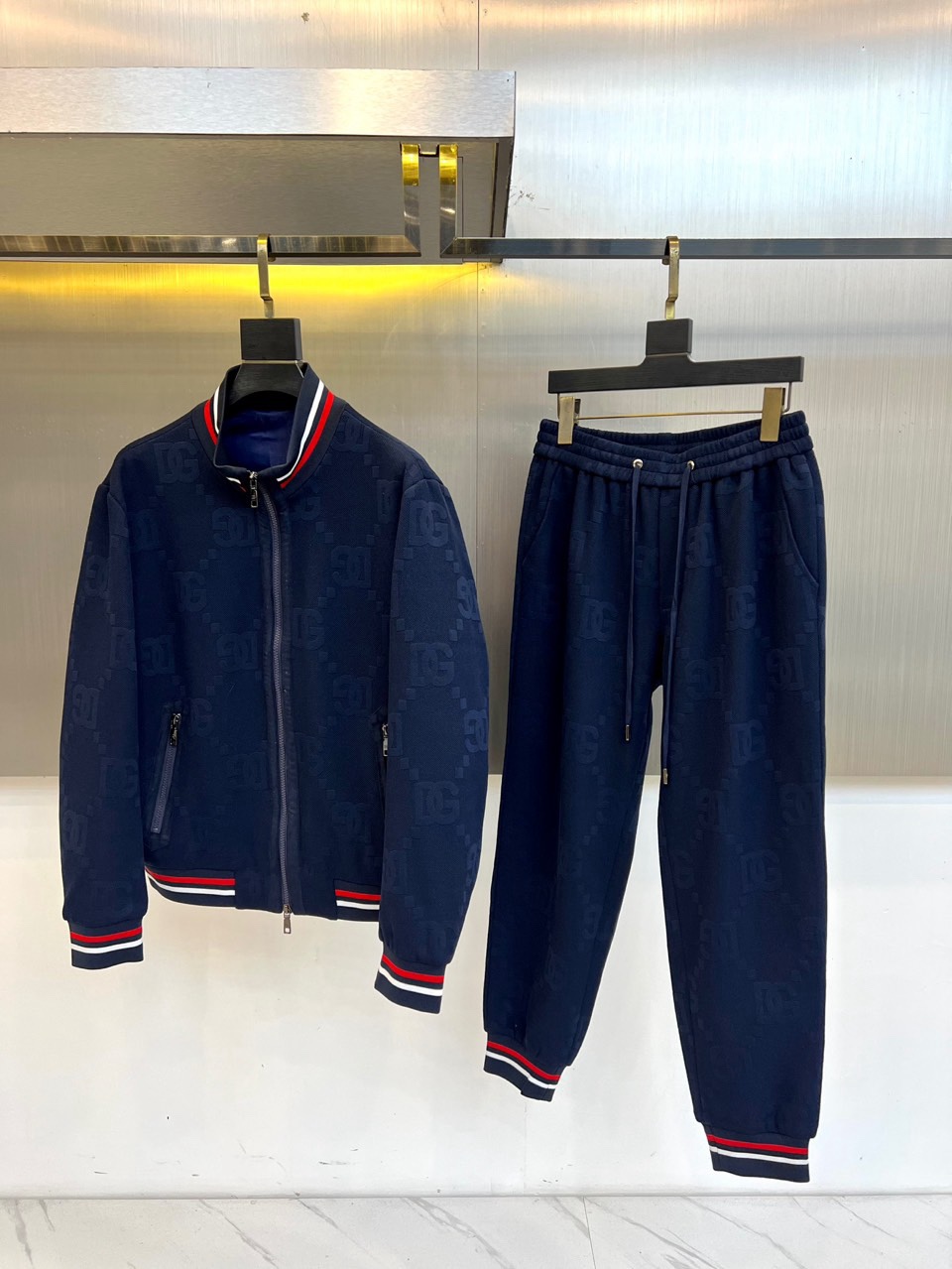 NO:712017,DG Dolce & Gabbana, 2025 autumn and winter new urban sports suit. A dark blue stand-collar zipper jacket and leggings trousers of the same color form an overall look. The body is covered with the brand's iconic dark pattern print, which is looming under the refraction of light, showing low-key luxury. The neckline  , cuffs and trousers are decorated with red, white and blue stripes, which are inspired by retro sports aesthetics and form a sharp visual collision with the main colors. The jacket is three-dimensional and equipped with a smooth zipper opening and closing system, and the trousers are equipped with an elastic drawstring waistband and side brand logo webbing.  The fabric is made of high-tech blended materials. The cotton base ensures skin-friendly breathability, and the elastic fiber enhances freedom of movement. It can be worn as a set to create a unified fashion sense, or it can be split and matched with other items. It is suitable for urban walks, social gatherings and other diverse scenes, through striped elements and dark  Echoing the pattern craftsmanship, it interprets GUCCI’s design philosophy of integrating Italian luxury genes with street sports style. 48-56 (model weighs 173,143 pounds, upper body size 50),, Dolce&Gabbana, gucci, jackets  & coats,19860909DG杜嘉班纳、2025秋冬新品都市运动套装.深蓝色立领拉链夹克与同色系束脚长裤组成整体造型,衣身满铺品牌标志性暗纹印花,在光线折射下若隐若现展现低调奢华.领口、袖口与裤脚均饰以红白蓝三色条纹,灵感源自复古运动美学,与主色调形成鲜明视觉碰撞.夹克采用立体剪裁搭配顺滑拉链开合系统,长裤配备弹性抽绳腰头与侧边品牌标识织带. 面料选用高科技混纺材质,棉质基底确保亲肤透气性,弹性纤维增强运动自由度.既可成套穿着打造统一时尚感,也可拆分搭配其他单品.适合都市漫步、社交聚会等多元场景,通过条纹元素与暗纹工艺的呼应,诠释GUCCI将意式奢华基因与街头运动风相融合的设计哲学.48-56（模特173,143斤上身50码）,,Dolce&Gabbana,gucci,jackets & coats,,Men's clothing