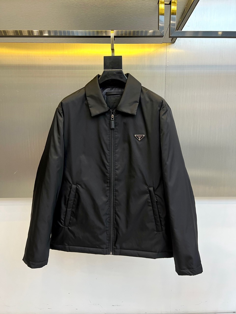 NO:712028,Prad (goose down), 2025 autumn and winter new product PRADA classic quilted down jacket.  The black stand-up collar is designed with a precision metal zipper system, and the body uses diamond-shaped quilting technology to lock down distribution. The left chest is embellished with the iconic triangular enamel badge, and the polished metal frame outlines the three-dimensional outline. The fabric is made of high-density windproof nylon, filled with a golden ratio of 90 white goose down and 10 feathers, and the down filling is accurately adapted to the severe cold environment of -5℃ to -15℃.  It can be paired with formal pants to create a business casual style, or with functional pants to create an urban outdoor look. From enamel badges to quilting technology, it interprets PRADA's design philosophy of integrating Italian aesthetics with practical protection. 48-56 (model 173,143 pounds, upper body size 50),, prada, prada, down jacket, gold,19860909Prad普拉（鹅绒）、2025秋冬新品 PRADA经典绗缝羽绒服. 黑色立领设计搭配精密金属拉链系统,衣身采用菱形绗缝工艺锁定羽绒分布.左胸点缀标志性三角形珐琅徽章,以抛光金属边框勾勒立体轮廓.面料选用高密度防风锦纶,内填充90白鹅绒与10羽毛的黄金配比,充绒量精准适配-5℃至-15℃严寒环境. 可搭配正装裤演绎商务休闲风格,或配合机能裤打造都市户外造型.从珐琅徽章到绗缝工艺,诠释PRADA将意式美学与实用防护相融的设计哲学.48-56（模特173,143斤上身50码）,,prada,prada,down jacket,gold,,Men's clothing