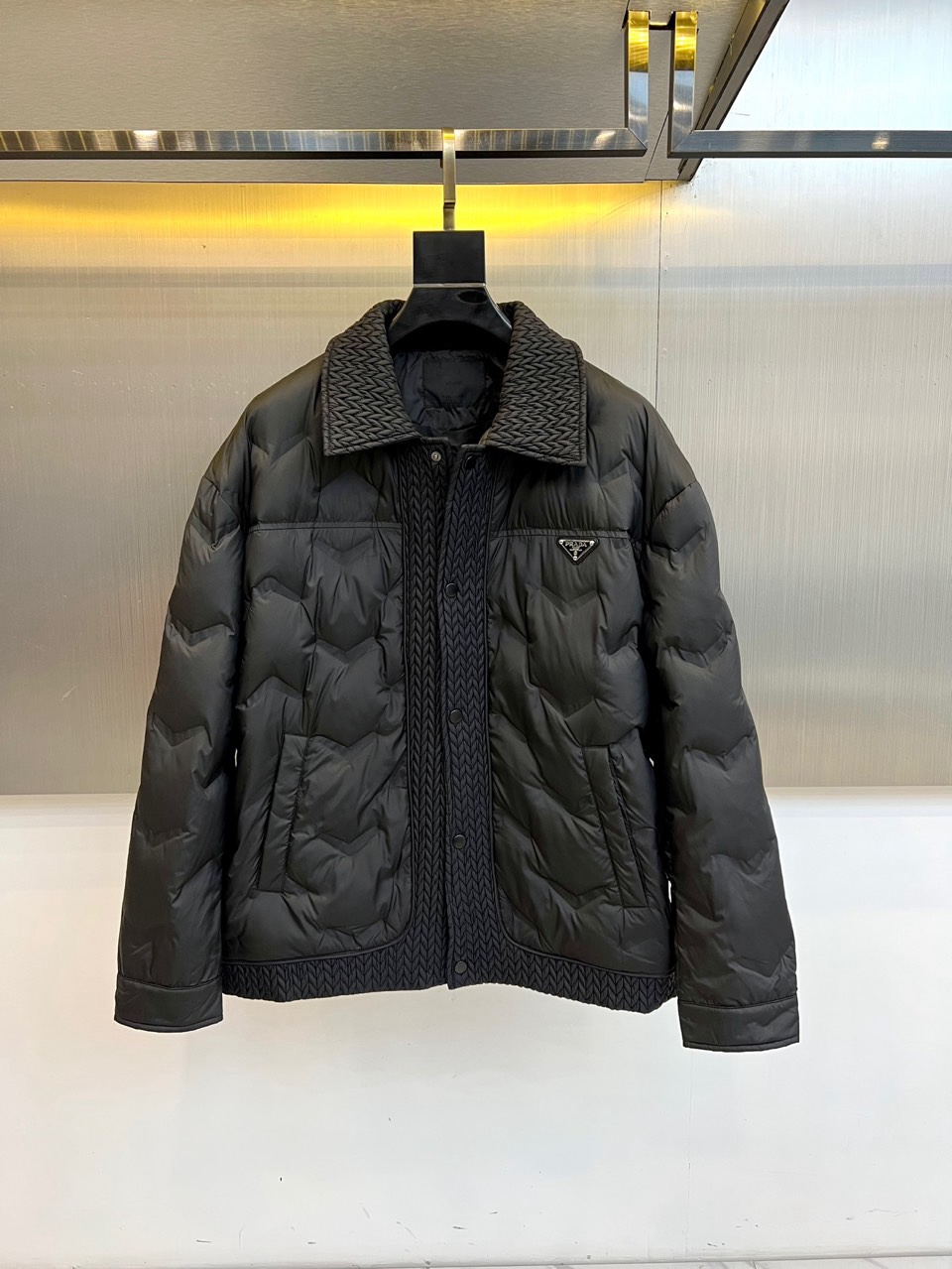 NO:712019,Prad, the new down jacket for autumn and winter 2025, this down jacket adopts a lapel design, the unique woven texture at the collar adds a delicate texture, and is paired with the brand's iconic triangular metal logo to highlight its identity. The body of the jacket is outlined with a three-dimensional outline through precise diamond-shaped pressing technology, which not only ensures even distribution of 90 white duck down but also enhances thermal insulation performance. The multi-pocket design cleverly combines practical functions with aesthetic balance.  The fabric is made of recycled fiber, and the collar accessories are also made of recycled fiber, reflecting the brand's commitment to environmental protection. Its design perfectly blends Italian elegance and pragmatism. The lapel shape can be paired with formal wear to show business temperament, or it can be combined with casual wear to create a fashionable winter look. Commuting from the city  For weekend trips, this down jacket, with Prada's unique exquisite craftsmanship and sustainable concept, has become a model of both temperature and style wisdom in the autumn and winter wardrobe. 48-56 (model is 173,143 pounds, upper body size 50),, prada, prada, down  jacket,19860909Prad普拉达、2025秋冬新款羽绒服,这款羽绒服采用翻领设计,领口处独特的编织纹理增添细腻质感,搭配品牌标志性三角形金属徽标彰显身份.衣身通过精准的菱形压线工艺勾勒立体轮廓,既确保90白鸭绒均匀分布又增强保暖性能.多口袋设计巧妙融合实用功能与美学平衡. 面料采用再生纤维材质,衣领配饰同样选用再生纤维,体现品牌对环保的承诺.其设计将意式优雅与实用主义完美融合,翻领造型可搭配正装展现商务气质,亦能结合休闲服饰打造冬日时尚造型.从都市通勤到周末出行,这件羽绒服以普拉达特有的精湛工艺与可持续理念,成为秋冬衣橱中兼具温度与风格智慧的典范之作.48-56（模特173,143斤上身50码）,,prada,prada,down jacket,,Men's clothing