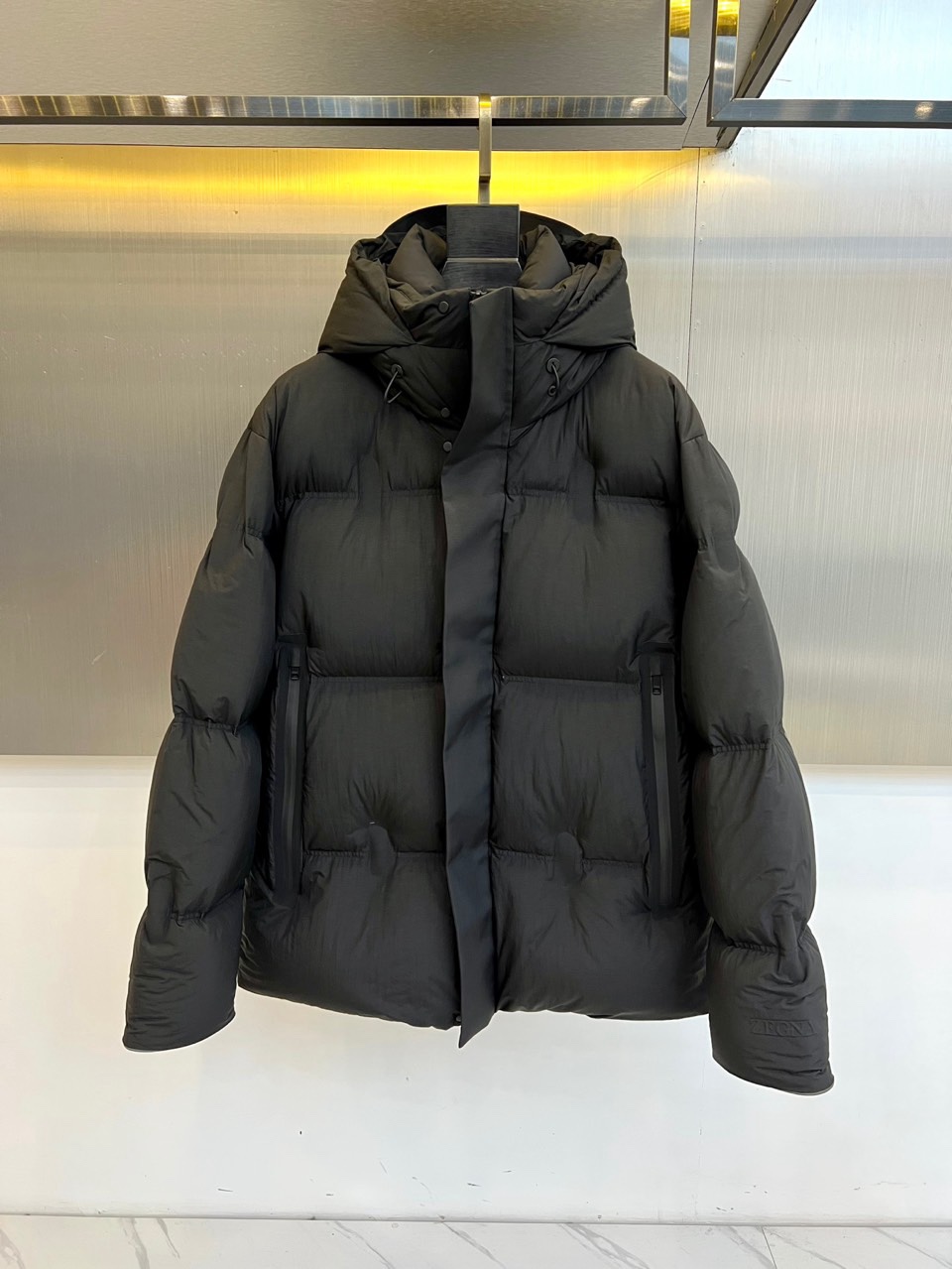 NO:712033,Zegna (goose down), the new down jacket for autumn and winter 2025, interprets contemporary casual style with a simple silhouette. The overall design is loose-cut black, with a hood and zipper opening to create a neat feel. The surface is run through with a delicate quilted checkered texture, giving the style layering and detail charm. The cuffs are decorated with brand logos, low-key highlighting the quality genes.  The fabric uses high-tech polyester fiber, which has excellent waterproof and windproof properties and is not afraid of bad weather. The lining is a combination of 91 nylon and 9 spandex, which combines warmth and elasticity and allows free movement. The secondary lining is also made of polyester fiber, which improves wearing comfort and durability. This down jacket will be practical  The combination of technology and simple aesthetics can provide light and reliable warmth protection whether it is daily life in the city or outdoor travel, interpreting the low-key and high-end fashion attitude in autumn and winter. 48-56 (model is 173,143 pounds, upper body size 50),,zegna,down  jacket,hats,19860909Zegna杰尼亚（鹅绒）、2025秋冬新品羽绒服,以简约轮廓演绎当代休闲风格.整体采用宽松剪裁的黑色设计,连帽与拉链开合营造利落感,表面贯穿精致的绗缝方格纹理,赋予造型层次与细节魅力.袖口饰有品牌标识,低调彰显品质基因. 面料运用高科技聚酯纤维,具备出色防水防风性能,无惧恶劣天气.里料融合91尼龙与9氨纶,兼顾保暖与弹性,活动自如.次里料同样采用聚酯纤维,提升穿着舒适度与耐久性.这款羽绒服将实用科技与简约美学相结合,无论是都市日常或户外出行,皆能提供轻盈而可靠的温暖防护,诠释秋冬低调而高级的时尚态度.48-56（模特173,143斤上身50码）,,zegna,down jacket,hats,,Men's clothing