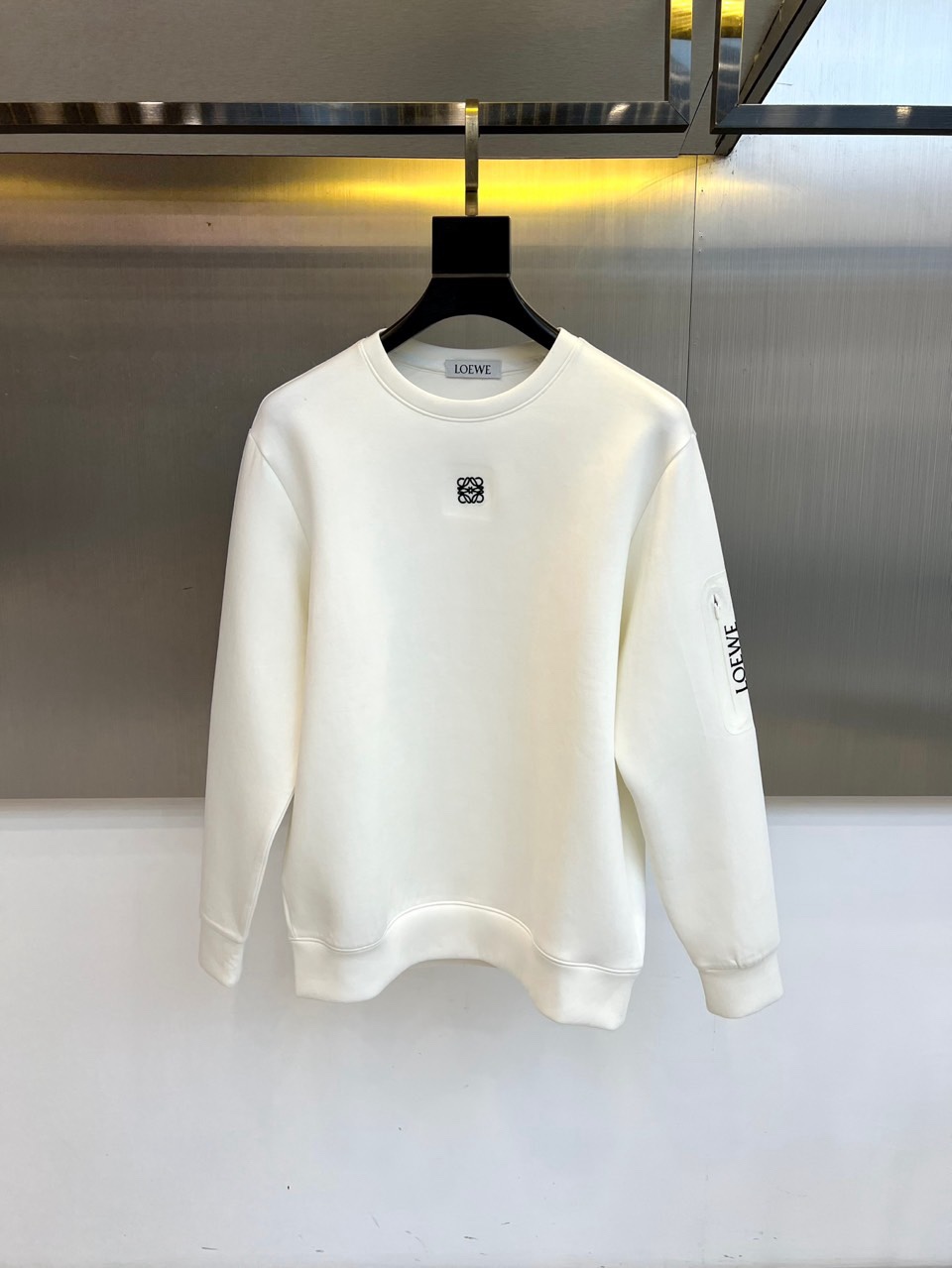 🌾罗意威、2025秋冬新款LOEWE白色圆领卫衣，以纯净白色调呈现，左胸饰有黑色品牌标志性图案，袖子上印