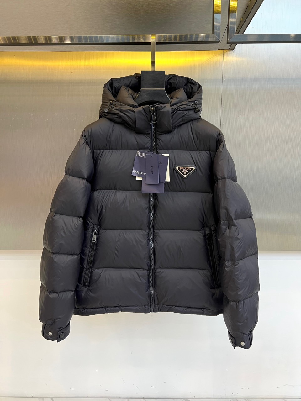 NO:730164,[Available for sale after the New Year] Prada, 2025 autumn and winter new product, black down jacket interprets simple and luxurious winter aesthetics. The style adopts a smooth knee-length silhouette, with a hooded design, which combines elegance and practical function. The neat lines run through the whole, and the iconic triangular metal logo is decorated on the front, becoming the visual focus and highlighting the brand identity. The smooth zipper extends from the collar to the hem, with hidden zipper pockets on both sides, and the cuffs are equipped with adjustable buttons. The details are full of ingenuity.  Its style is a fusion of modern minimalism and high fashion. Pure black and slender tailoring create a calm and powerful urban image. The core technology uses environmentally friendly materials, the outer fabric is recycled polyamide fiber, and the lining and liner also use recycled materials, reflecting the brand concept of sustainable luxury. It is filled with 90% high-quality white duck down, with a down filling capacity of 161 grams, ensuring excellent lightness and warmth.  This down jacket is the ultimate investment for your winter wardrobe. It can not only resist the severe cold, but also easily enhance the sense of luxury and recognition of the overall look. It is perfectly suitable for a variety of occasions from urban commuting to leisure travel. 48-56 (model is 173,143 pounds, upper body size 50),, prada, prada, down jacket, hats,19860909【可年后售后】 Prad普拉达、2025秋冬新品,黑色羽绒服诠释简约奢华的冬日美学.款式采用流畅的过膝廓形,搭配连帽设计,兼具优雅气场与实用功能.利落的线条贯穿整体,正面饰有标志性三角形金属徽标,成为视觉焦点,彰显品牌身份.顺滑拉链从领口延伸至下摆,两侧设有隐藏式拉链口袋,袖口配备可调节纽扣,细节尽显匠心. 其风格是现代极简主义与高级时装的融合.纯粹的黑色与修长剪裁,塑造出冷静而强大的都市形象.核心技术采用环保材质,外部面料为再生聚酰胺纤维,里料与内胆亦使用再生材料,体现可持续奢华的品牌理念.填充90高品质白鸭绒,充绒量达161克,确保卓越的轻盈保暖性. 这件羽绒服是冬日衣橱的终极投资,既能抵御严寒,又能轻松提升整体造型的高级感与辨识度,完美适配从都市通勤到休闲出行的多种场合.48-56（模特173,143斤上身50码）,,prada,prada,down jacket,hats,,Men's clothing