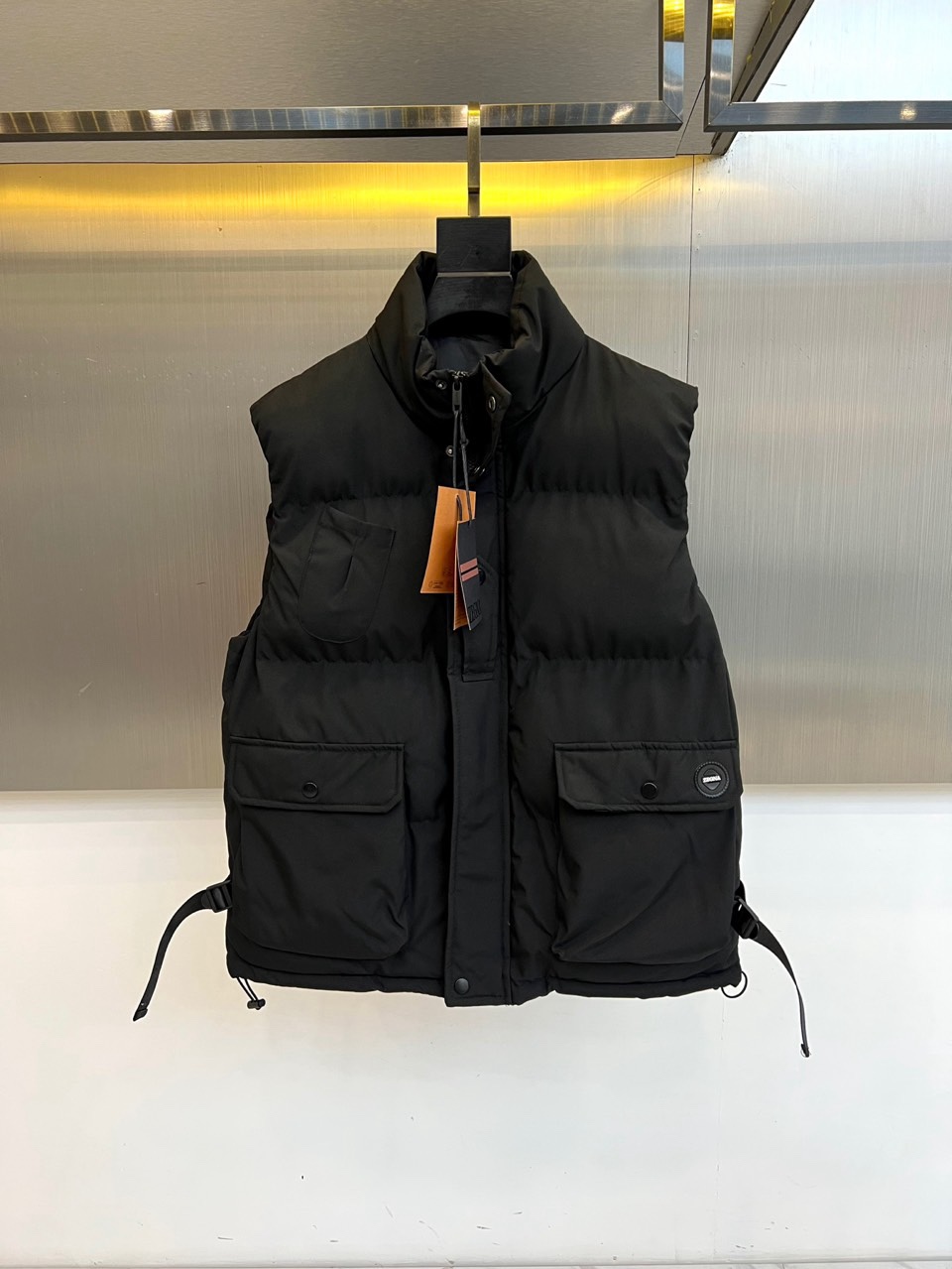 NO:730142,[After-sales service is available after the new year]  Zegna, the 2025 autumn and winter down vest, uses classic black to interpret timeless fashion. In terms of style, it is filled with light and warm down, and the stand-up collar design is neat and stylish. The front uses a smooth zipper opening and closing, making it easy to put on and take off. There are three-dimensional large-capacity pockets on both sides, decorated with exquisite round brand logos, which are both practical and decorative. The built-in adjustable drawstring on the side can flexibly outline or relax the fit, ensuring a good fit and freedom of movement.  Its style perfectly combines simple practicality and Italian elegance. Pure black and neat tailoring highlight the calm and elegant classic style, while the exquisite detailed design injects modernity and advanced craftsmanship. It can be worn with a shirt and a suit to show a calm style during business commuting; it can also be paired with a turtleneck sweater and casual pants for weekends.  Time interprets a comfortable and elegant attitude towards life. This vest is not only a practical choice to resist the cold, but also a key item to enhance the overall style and texture. It shows the style of a modern gentleman in simplicity. 48-56 (model is 173,143 pounds, upper body size 50),,zegna,shirts,down  jacket, business suit,19860909【可年后售后】 Zegna杰尼亚、2025秋冬羽绒马甲,以经典黑色演绎隽永风尚.款式上,甄选轻盈保暖的羽绒填充,立领设计利落有型.前襟采用顺滑拉链开合,便捷穿脱.两侧设有立体大容量口袋,饰以精致圆形品牌标志,兼具实用与装饰性.侧身内置可调节抽绳,能灵活勾勒或放松版型,确保贴合身型与活动自由度. 其风格完美融合了简约实用与意式优雅.纯粹的黑色与利落剪裁,彰显沉稳大气的经典风范,而精巧的细节设计则注入现代感与高级工艺气息.它既能内搭衬衫与西装,在商务通勤中展现从容型格；亦可搭配高领针织衫与休闲裤,于周末时光诠释舒适而考究的生活态度.这件马甲不仅是抵御寒意的实用之选,更是提升整体造型层次与质感的关键单品,于简约中尽显现代绅士风度.48-56（模特173,143斤上身50码）,,zegna,shirts,down jacket,business suit,,Men's clothing