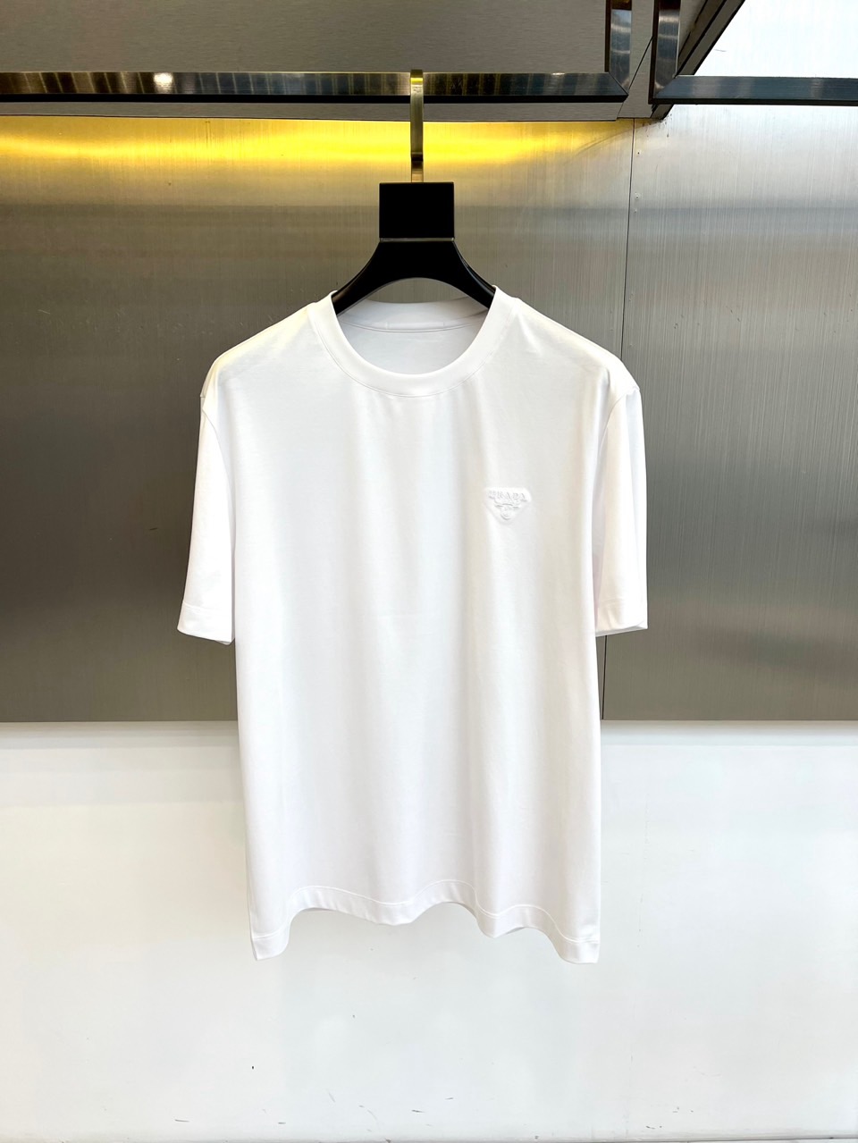 NO:732948,Prada, the new men's T-shirt for spring and summer 2026, interprets simple and modern casual aesthetics with a classic round neck and loose short-sleeved silhouette. The highlight of its design is the three-dimensional brand triangle logo decorated on the left chest, which is created with exquisite layers through exquisite craftsmanship, becoming a low-key and eye-catching status symbol.  The core of this product lies in the innovative blended fabric selected from 66% cotton, 25% polyester and 9% mulberry silk. The ice-like cotton is soft and comfortable against the skin. The polyester ensures a crisp and durable fit, while the addition of mulberry silk gives the fabric a natural luster, excellent breathability and extraordinary smooth touch, which together create a unique and extremely comfortable spring and summer wearing experience.  The overall tailoring focuses on a relaxed sense of space and abandons complicated decoration. It perfectly combines high-end materials with minimalist design. It can be worn alone to show a casual style, or as an inner layer to enhance the texture of the overall shape, accurately conveying Prada's restrained and advanced fashion language. M-4XL (model weighs 173,143 pounds, upper body size L),, prada, prada, T-shirt, tees, t-shirt,19860909Prad普拉达、2026春夏新品男士T恤,以经典圆领与宽松短袖廓形,诠释简约现代的休闲美学.其设计亮点在于左胸位置装饰的立体品牌三角徽标,通过精湛工艺打造出细腻层次,成为低调而瞩目的身份象征. 本品核心在于创新混纺面料甄选66棉、25涤纶与9桑蚕丝匠心融合.冰感棉柔亲肤舒适.涤纶确保版型挺括与耐久性,而桑蚕丝的加入则赋予了面料天然的光泽感、卓越的透气性与非凡的顺滑触感,共同成就了独具一格且极度舒适的春夏穿着体验. 整体剪裁注重松弛有度的空间感,摒弃繁复装饰.它将高端材质与极简设计完美结合,既能单独穿着展现随性型格,亦可作为内搭提升整体造型的质感,精准传递普拉达克制而高级的时尚语言.M-4XL（模特173,143斤上身L码）,,prada,prada,T-shirt,tees，t-shirt,,Men's clothing