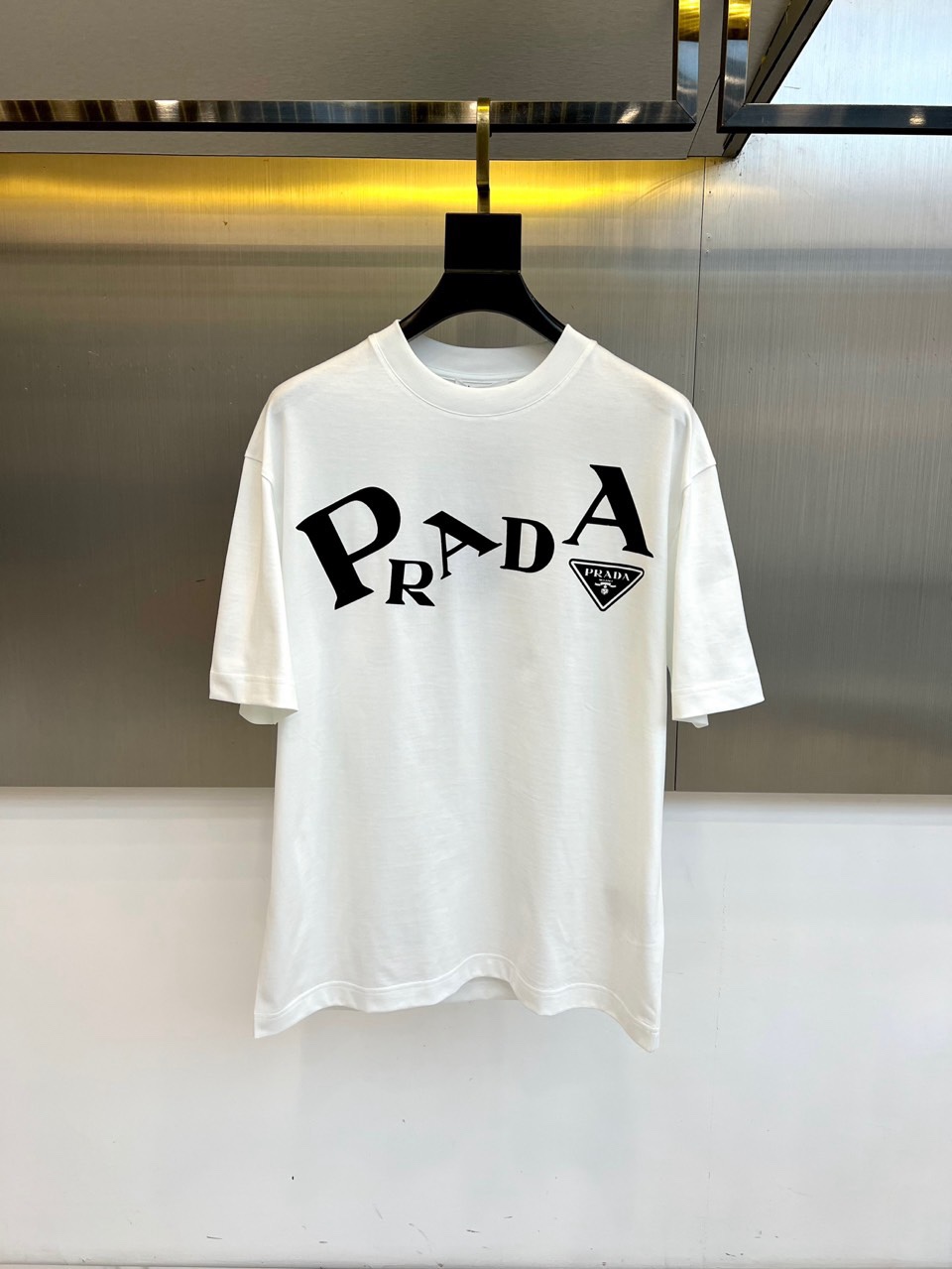 NO:734842,Prad, 2026 spring and summer T-shirts are presented in a classic round neck short-sleeved silhouette, setting a pure tone. The core of the design focuses on the eye-catching brand logo on the front of the clothes. The letters are engraved on it in a unique shape and proportion, which is highly visual and artistic. The iconic triangle logo is supplemented in the lower right corner. The exquisite details highlight the brand identity. The overall style cleverly combines the rigorous craftsmanship and precision of high-end fashion houses.  The free and easy attitude of street fashion exudes a strong aura in simplicity. Whether paired with exquisite bottoms or casual items, you can easily create an urban look with both personality and taste, becoming an indispensable iconic item this season. 48-56 (model weighs 173,143 pounds, upper body size 50),, prada, prada, T-shirt, tees, t-shirt,19860909Prad普拉达、2026春夏T恤以经典圆领短袖廓形呈现,奠定纯粹基调.设计核心聚焦于衣身正面醒目的品牌标识,字母以独特的形态与比例镌刻其上,极具视觉张力与艺术感,右下角辅以标志性三角徽标,精致细节彰显品牌身份.整体风格巧妙融合了高端时装屋的严谨工艺与街头潮流的洒脱态度,简约中透出强大气场.无论是搭配精致下装或休闲单品,都能轻松塑造兼具个性与品味的都市造型,成为本季不可或缺的标志性单品.48-56（模特173,143斤上身50码）,,prada,prada,T-shirt,tees，t-shirt,,Men's clothing