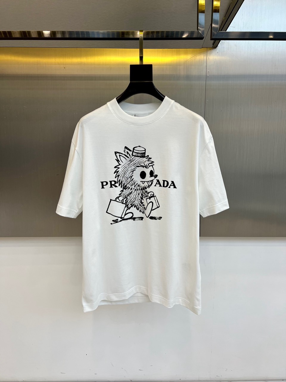 NO:734827,Prada, the new T-shirt for spring and summer 2026, is presented with a classic round neck and neat short-sleeved silhouette. The design focuses on the unique hand-painted style pattern on the chest. The plush cartoon image of a handbag is full of fun, cleverly integrated with the brand's classic logo, and collides with fresh artistic sparks. This design breaks the traditional framework and perfectly combines exquisite craftsmanship with playful childlike innocence. The overall style is bold and innovative  , while continuing the brand's high-end genes, it injects a relaxed and energetic street atmosphere. It is not only a T-shirt, but also a fashion statement that expresses individual attitude, helping you easily control various casual social occasions and show a unique fashion sense. 48-56 (model 173, 143 pounds, upper body size 50),, prada, prada, T-shirt, tees, t-shirt,19860909Prad普拉达、2026春夏新品T恤,以经典圆领与利落短袖廓形呈现.设计焦点集中于胸前独具匠心的手绘风格图案,一个手提袋子的毛绒卡通形象趣味十足,与品牌经典标识巧妙融合,碰撞出鲜活的艺术火花.这种设计打破了传统框架,将精湛工艺与玩味童心完美结合.整体风格大胆创新,在延续品牌高端基因的同时,注入轻松活力的街头气息.它不仅是件T恤,更是表达个性态度的时尚宣言,助你轻松驾驭各种休闲社交场合,展现与众不同的时尚触觉.48-56（模特173,143斤上身50码）,,prada,prada,T-shirt,tees，t-shirt,,Men's clothing