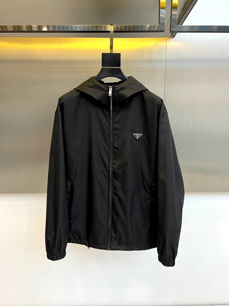 NO:734849,Prada, the 2026 spring and summer series hooded jacket interprets urban functional aesthetics with a simple silhouette and practical details. The iconic inverted triangle metal logo is embellished on the left chest, highlighting the brand identity. The hooded design combines casualness and protection, with smooth zipper opening and closing, making it easy to put on and take off. The overall cut is neat and smooth, with clear shoulder lines, taking into account loose comfort and a stylish silhouette.  This product is made of high-performance windproof fabric, with a texture that is crisp and breathable, adapting to the changeable weather in spring and summer. The functional details are refined and the three-dimensional pockets on both sides provide convenient storage, and the cuffs and hem are gathered in to enhance the fit. Its style walks between street fashion and pragmatism, transforming workwear inspiration into exquisite daily wear.  Whether paired with denim pants to create a casual look, or layered with sports-style bottoms, it can easily be used in various scenarios, becoming a must-have item to cope with seasonal transitions and enhance the level of dressing. 48-56 (model weighs 173,143 pounds, upper body size 50),, prada, prada, jackets & coats, hats,19860909Prad普拉达、2026春夏系列连帽夹克,以简约廓形与实用细节诠释都市机能美学.标志性倒三角形金属徽标点缀于左胸,彰显品牌身份.连帽设计融合休闲感与防护性,配合顺滑拉链开合,穿脱便捷.整体剪裁利落流畅,肩线清晰,兼顾宽松舒适与有型轮廓. 本品选用高性能防风面料,质地挺括且透气,适应春夏多变天气.功能性细节精炼两侧立体插袋提供储物便利,袖口与下摆的收束设计增强贴合度.其风格游走于街头潮流与实用主义之间,将工装灵感转化为精致日常着装. 无论是搭配丹宁裤塑造休闲造型,或与运动风格下装叠穿,皆能轻松驾驭多元场景,成为应对季节过渡、提升穿搭层次的必备单品.48-56（模特173,143斤上身50码）,,prada,prada,jackets & coats,hats,,Men's clothing