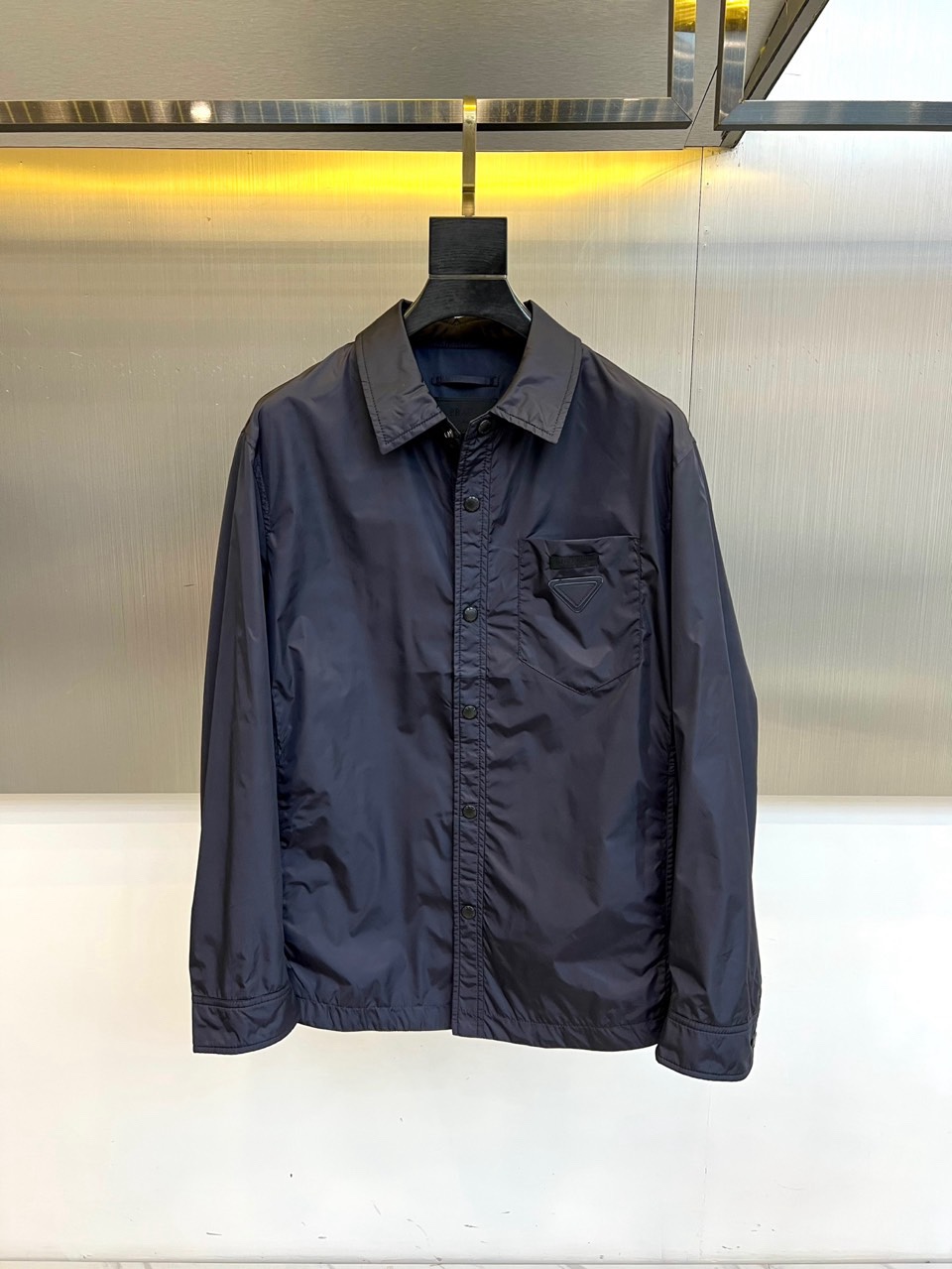 Prad普拉达、2026春夏男士夹克，以简约线条重塑都市机能美学。款式采用衬衫式翻领与利落宽松剪裁，门襟