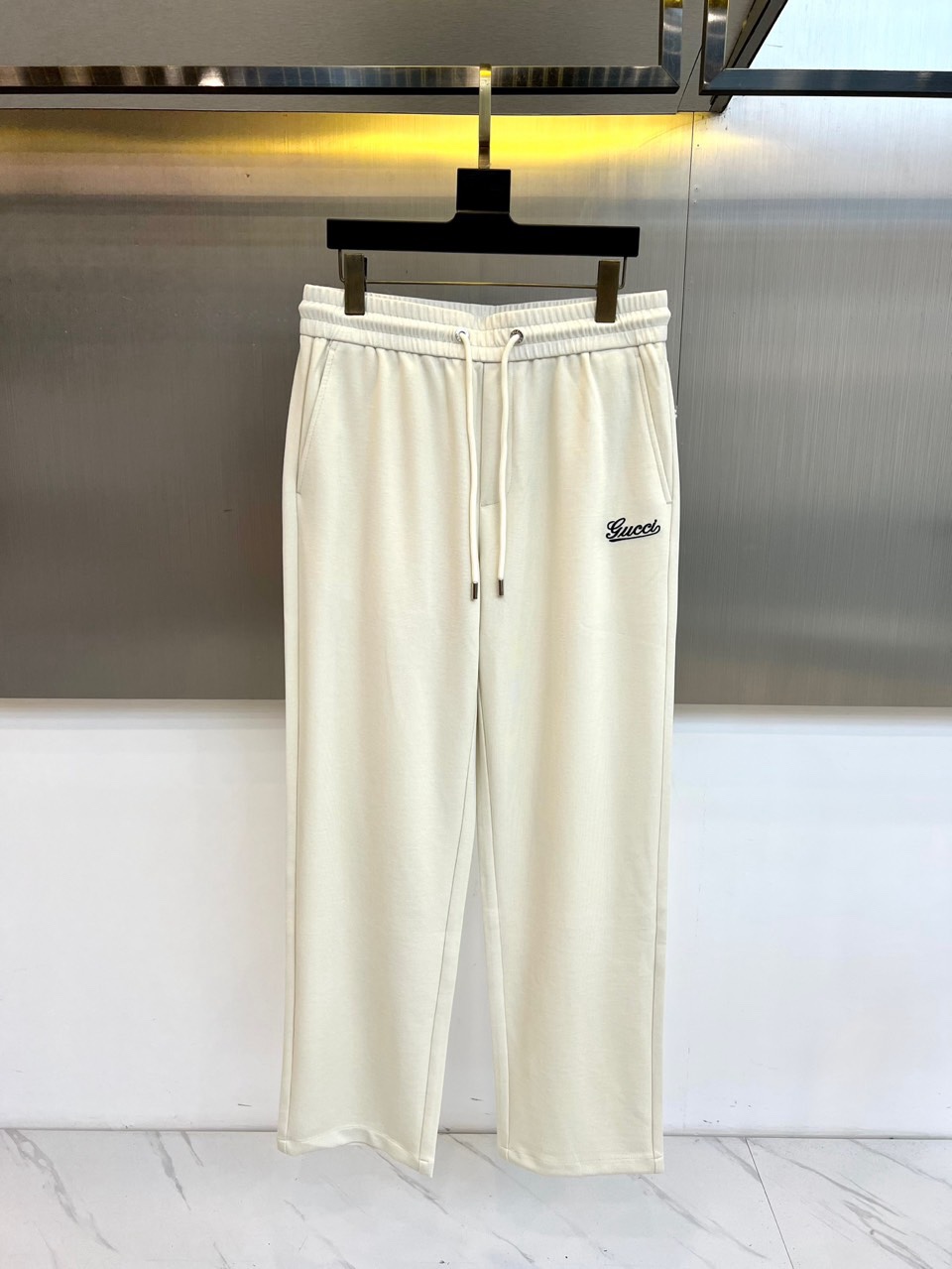 Gucc古驰、2026春夏男士休闲裤，以宽松剪裁重塑当代休闲美学。标志性设计在于裤身正面醒目的品牌刺绣标