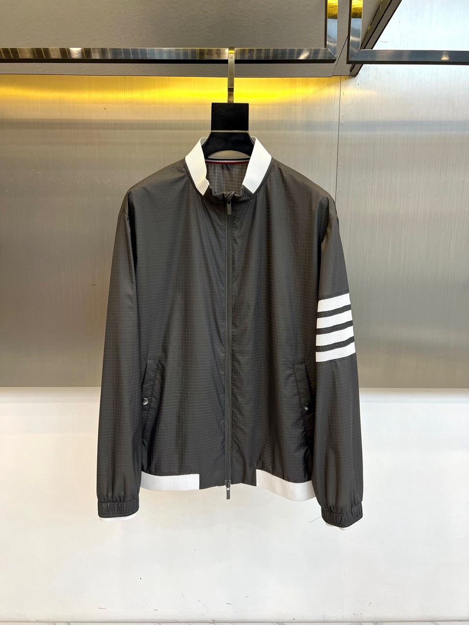 TB汤姆布朗、2026春夏新品夹克，以利落棒球领设计开篇，罗纹领口、下摆与袖口形成经典撞色，袖身四条条纹