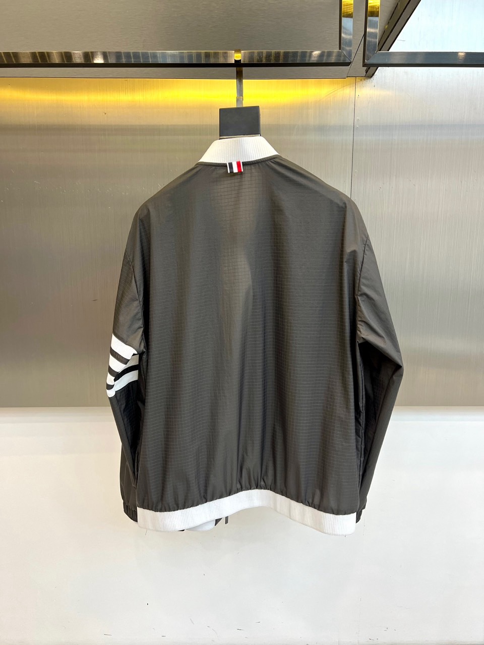 TB汤姆布朗、2026春夏新品夹克，以利落棒球领设计开篇，罗纹领口、下摆与袖口形成经典撞色，袖身四条条纹