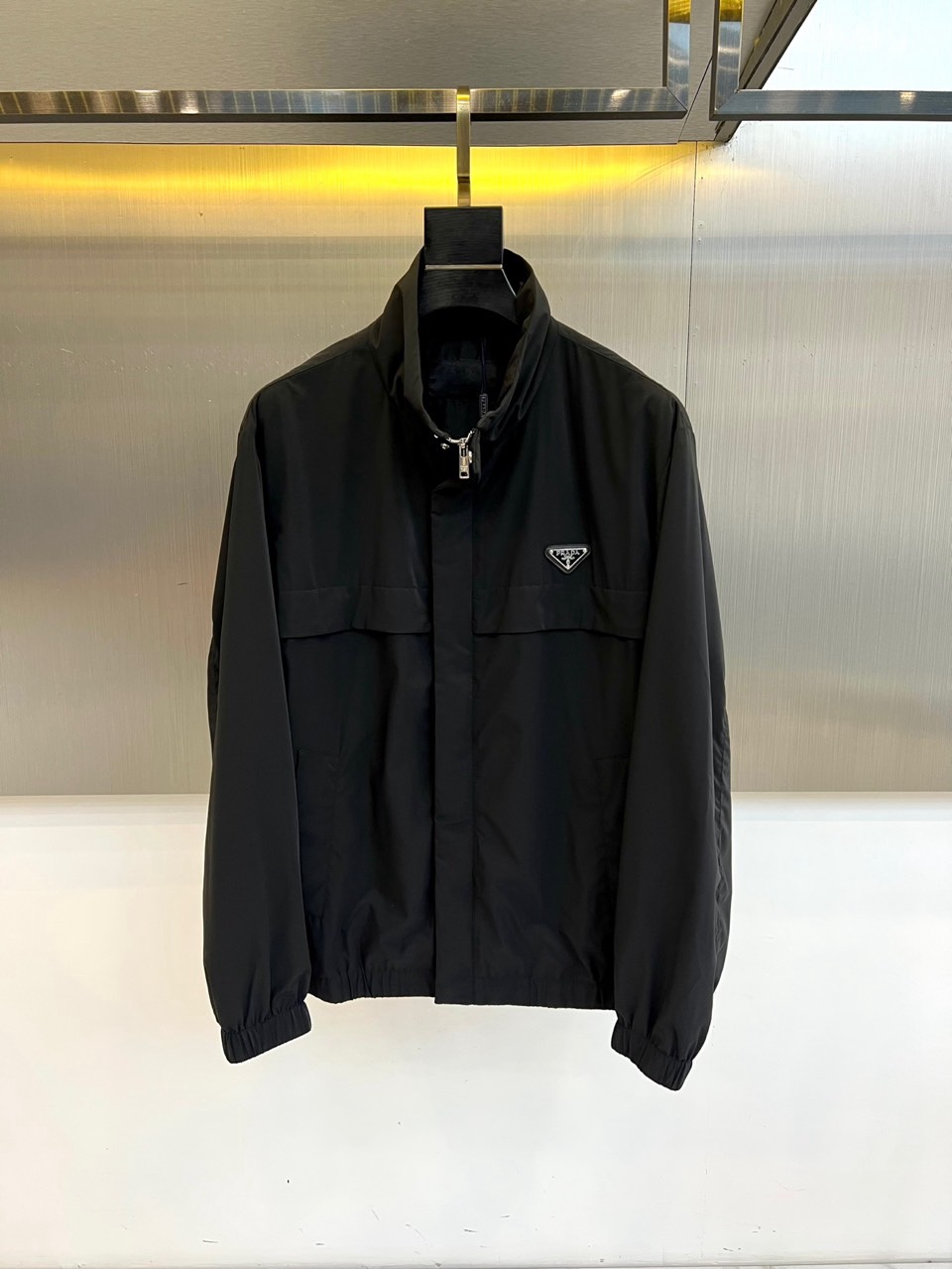 Prad普拉、2026春夏新品男士夹克，以简约立领设计勾勒利落廓形。胸前点缀标志性的金属三角徽标，于极简